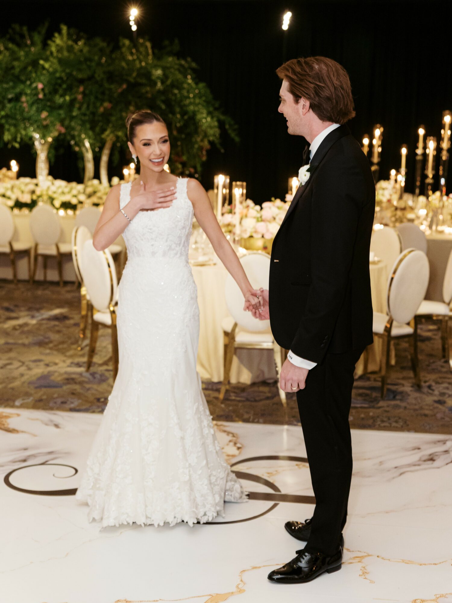 A bride and groom holding hands and smiling at each other in a decorated wedding reception hall.