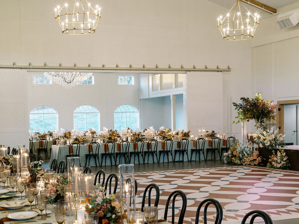 Elegant banquet hall with long table, floral arrangements, chandeliers, and a patterned dance floor, set for a celebration.