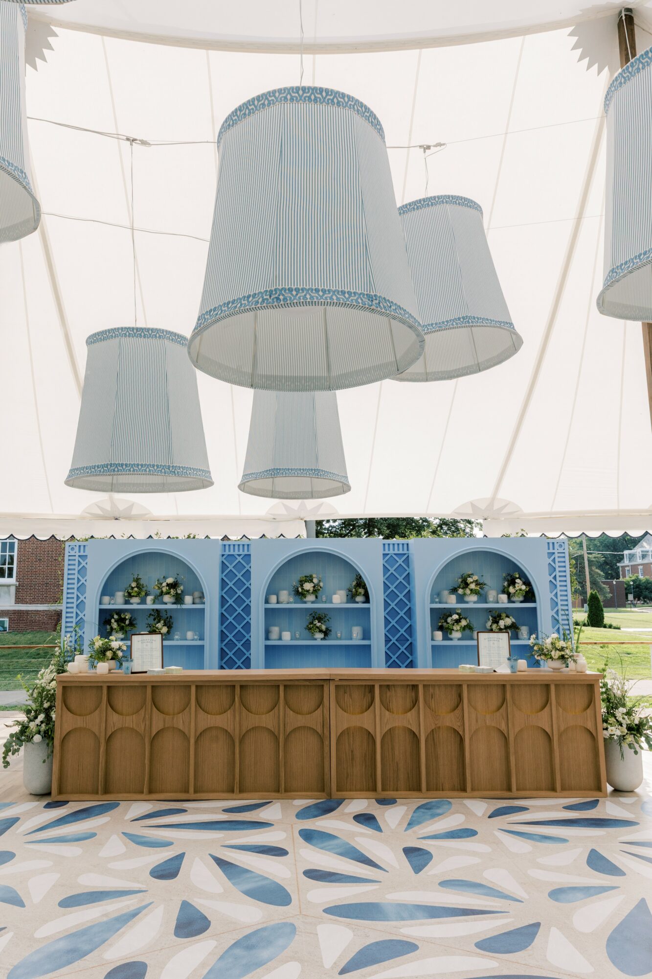 Ceiling with hanging blue and white lampshades, and a room with blue shelves, a brown sofa, and a patterned floor.