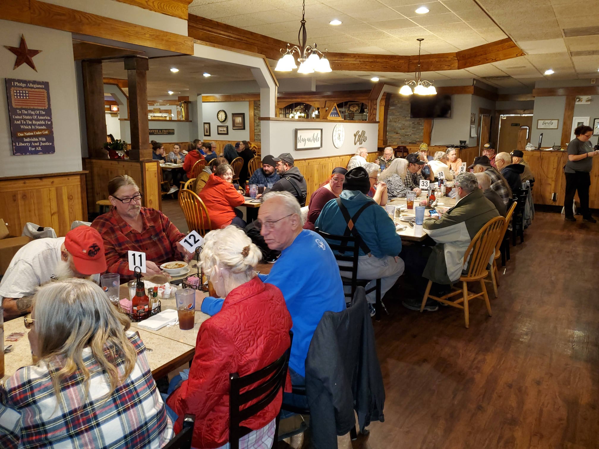 People dining at tables in a restaurant with wooden accents and a bar area in the background.