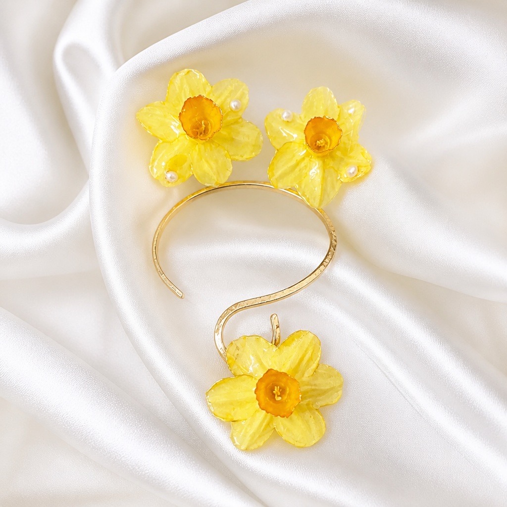 Gold bracelet with three yellow flower decorations on white satin fabric, one flower at the end and two on the band.