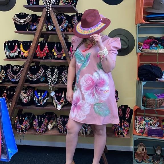 Child in pink floral dress and wide-brimmed hat shopping for jewelry, shelves with necklaces behind her.