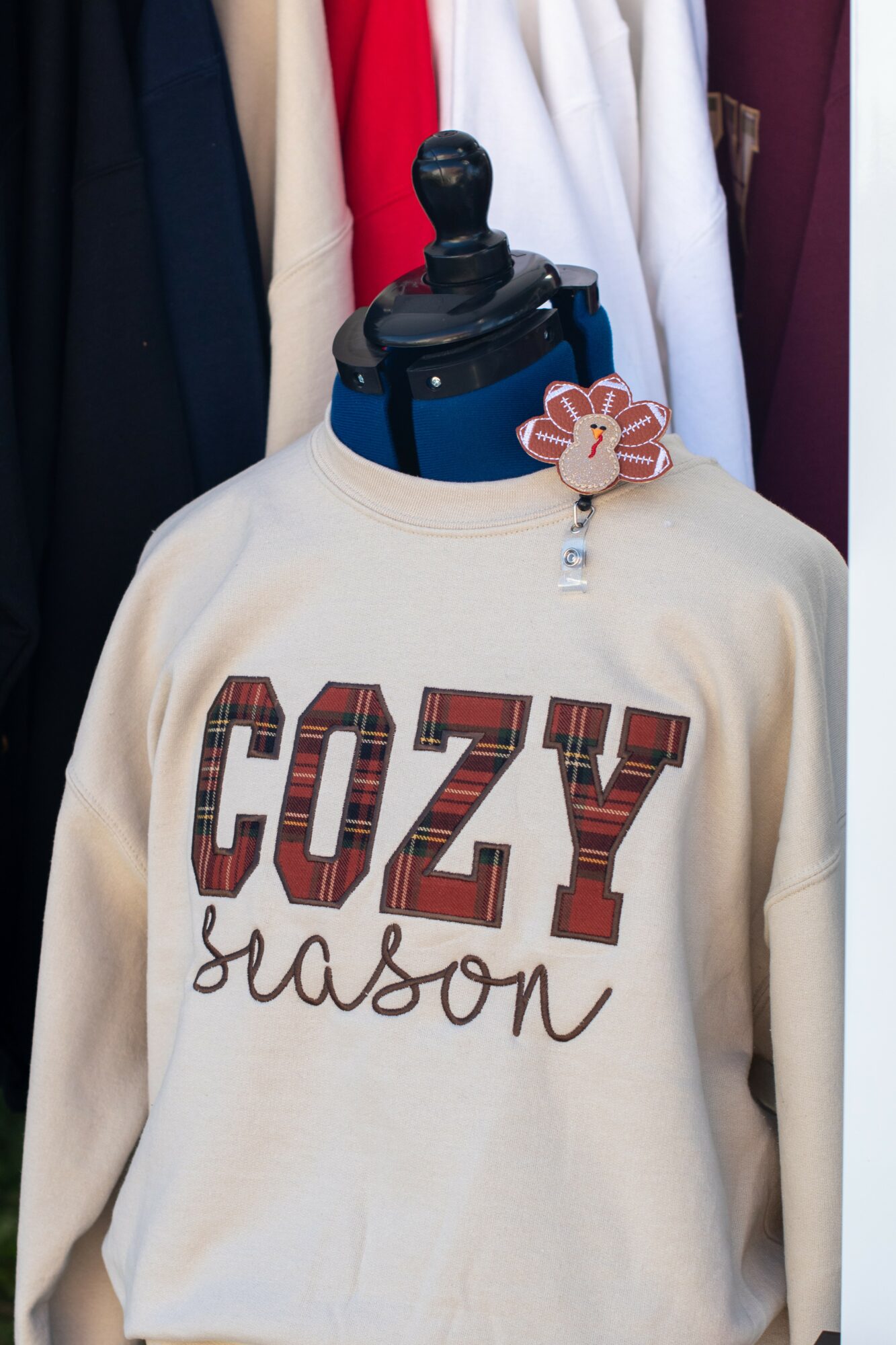 Sweater with 'COZY season' text displayed on a mannequin, surrounded by hanging clothes.