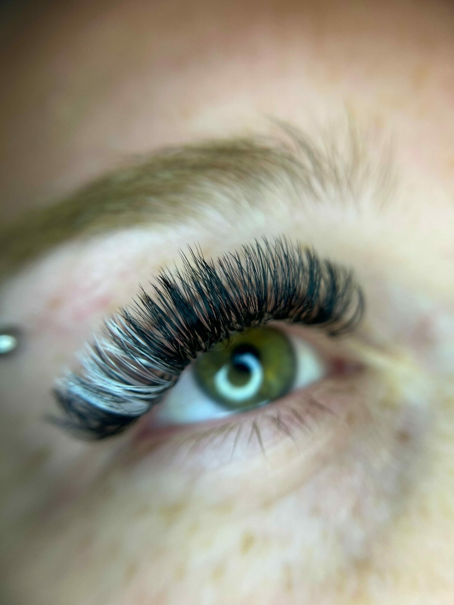 Close-up of a person's eye with long, dark eyelashes and a green iris, looking upward.