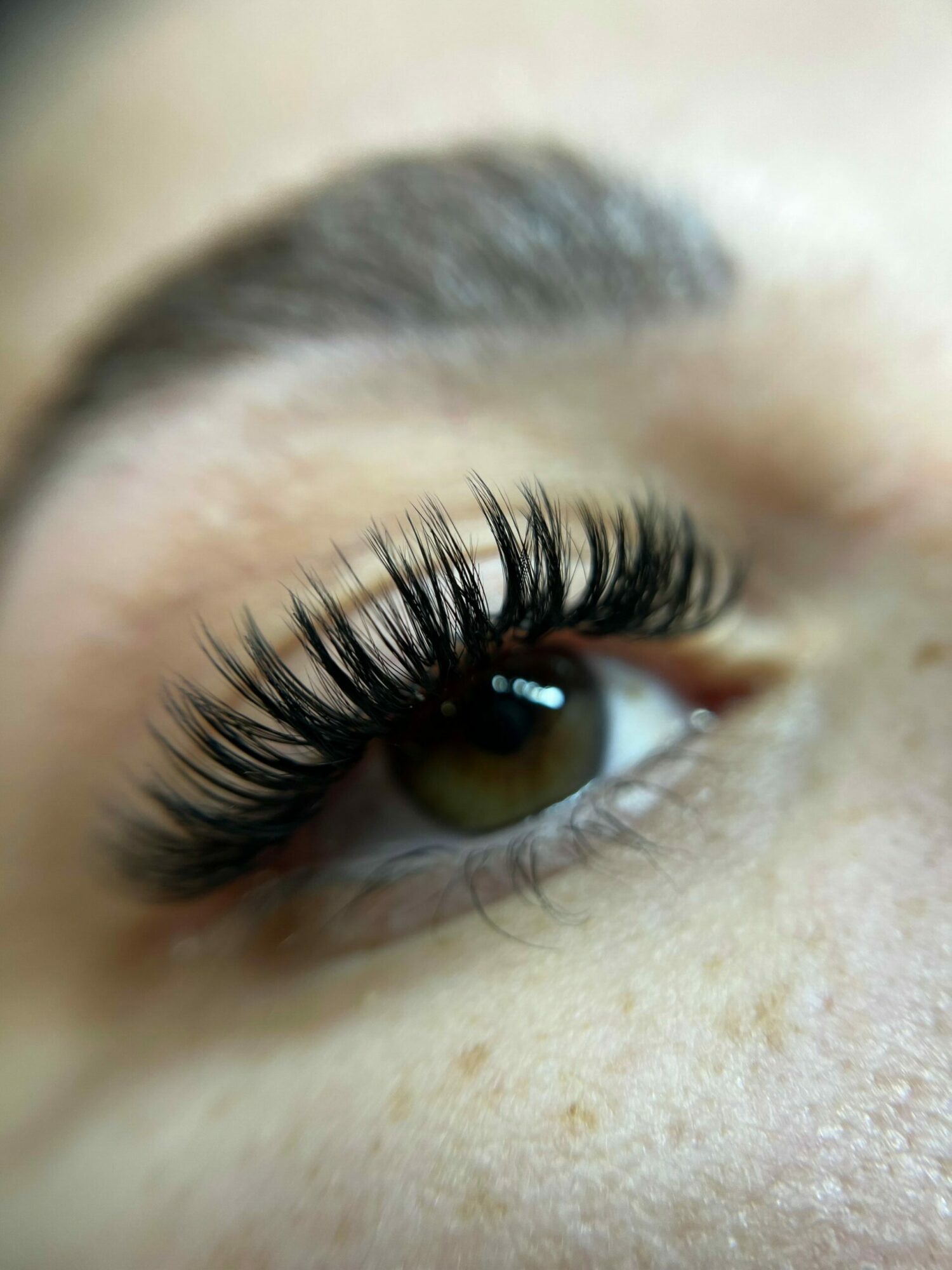 Close-up of a person's eye with long, curled eyelashes and visible eyebrow hair.