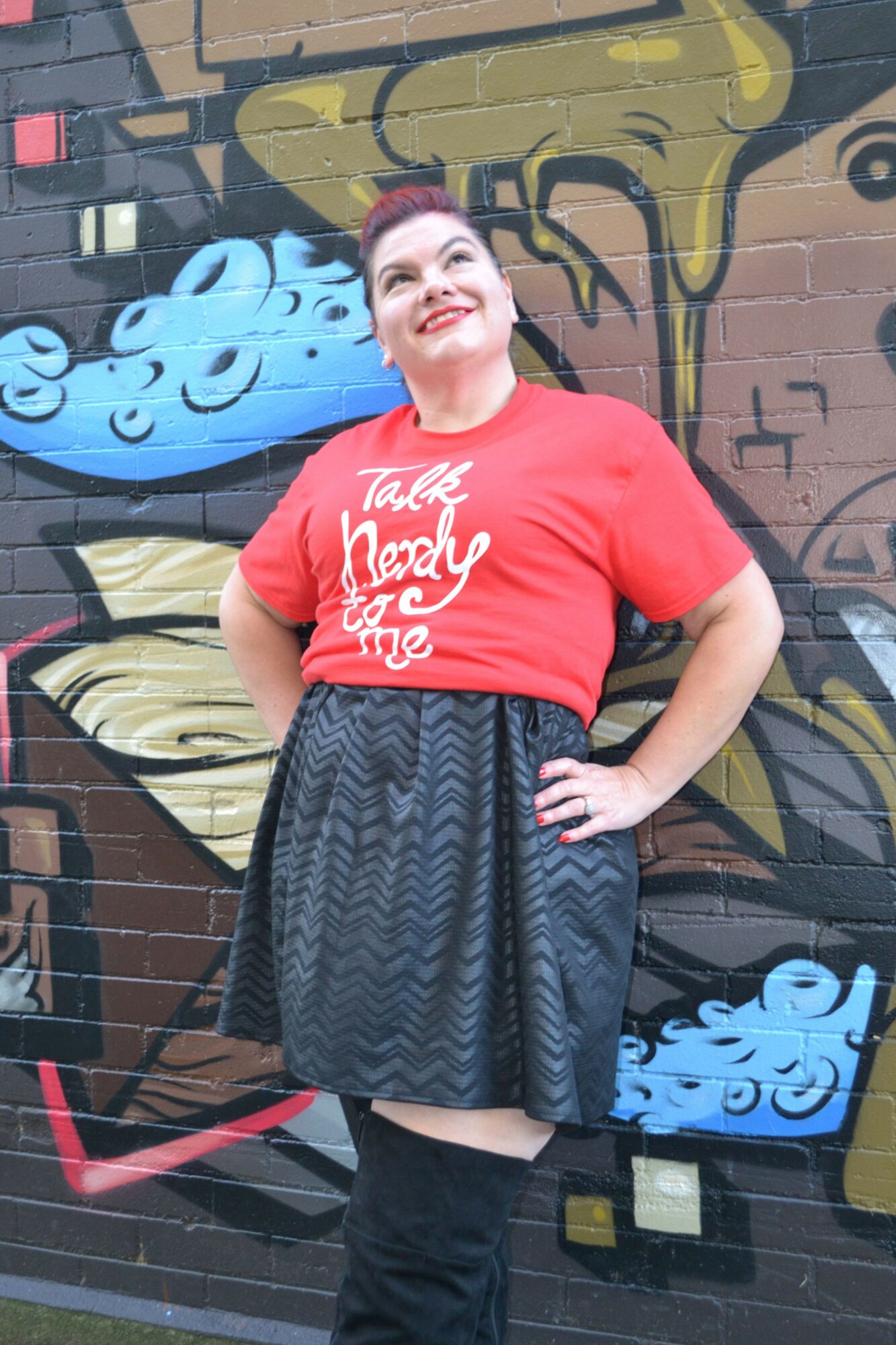 Person standing in front of a colorful graffiti wall, wearing a red T-shirt and dark pants, smiling.
