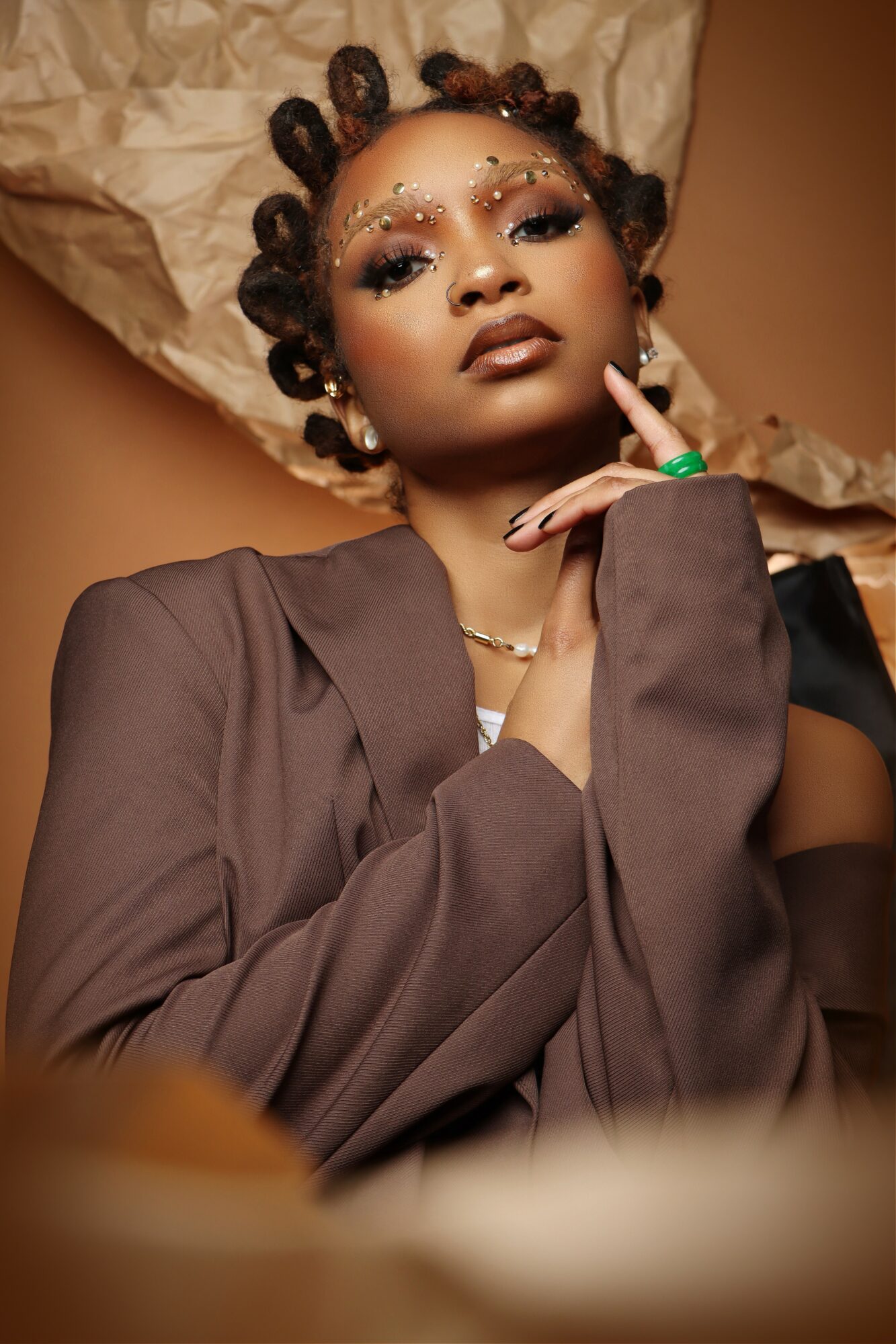 Portrait of a woman with styled hair, makeup, and jewelry, wearing a dark blazer, posing with her hand near her face.