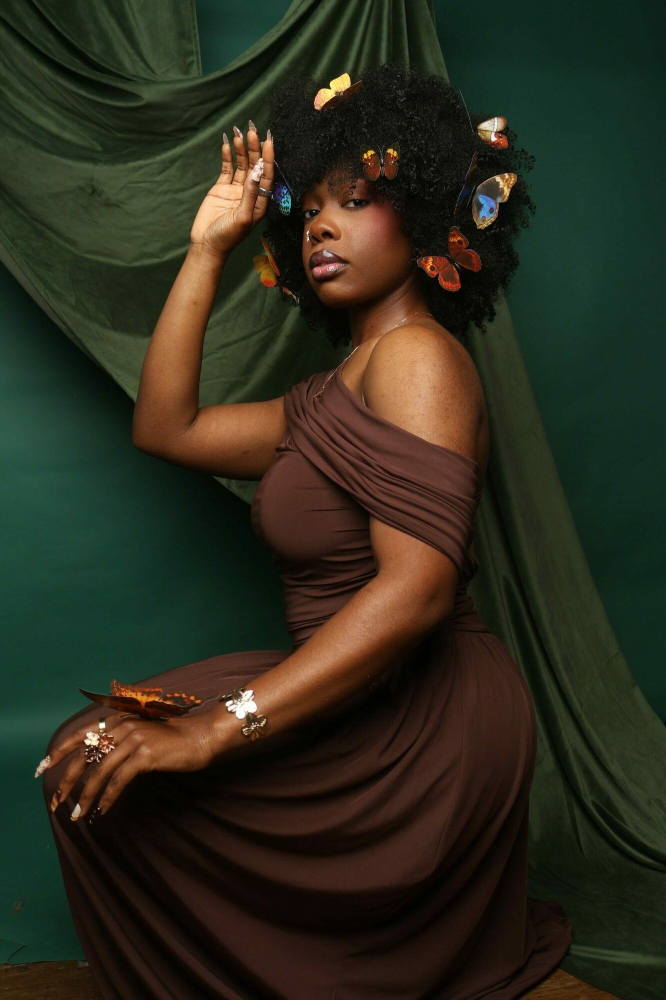 Woman lying on a green velvet surface with colorful hair accessories, wearing a brown dress, looking at the camera.