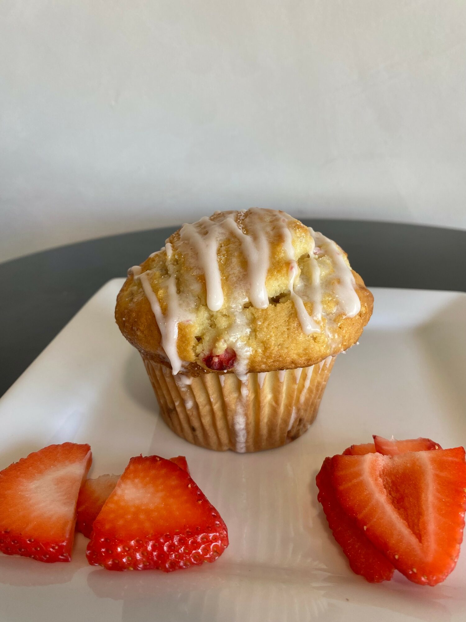 A muffin with white icing and strawberries on a white plate against a plain background.