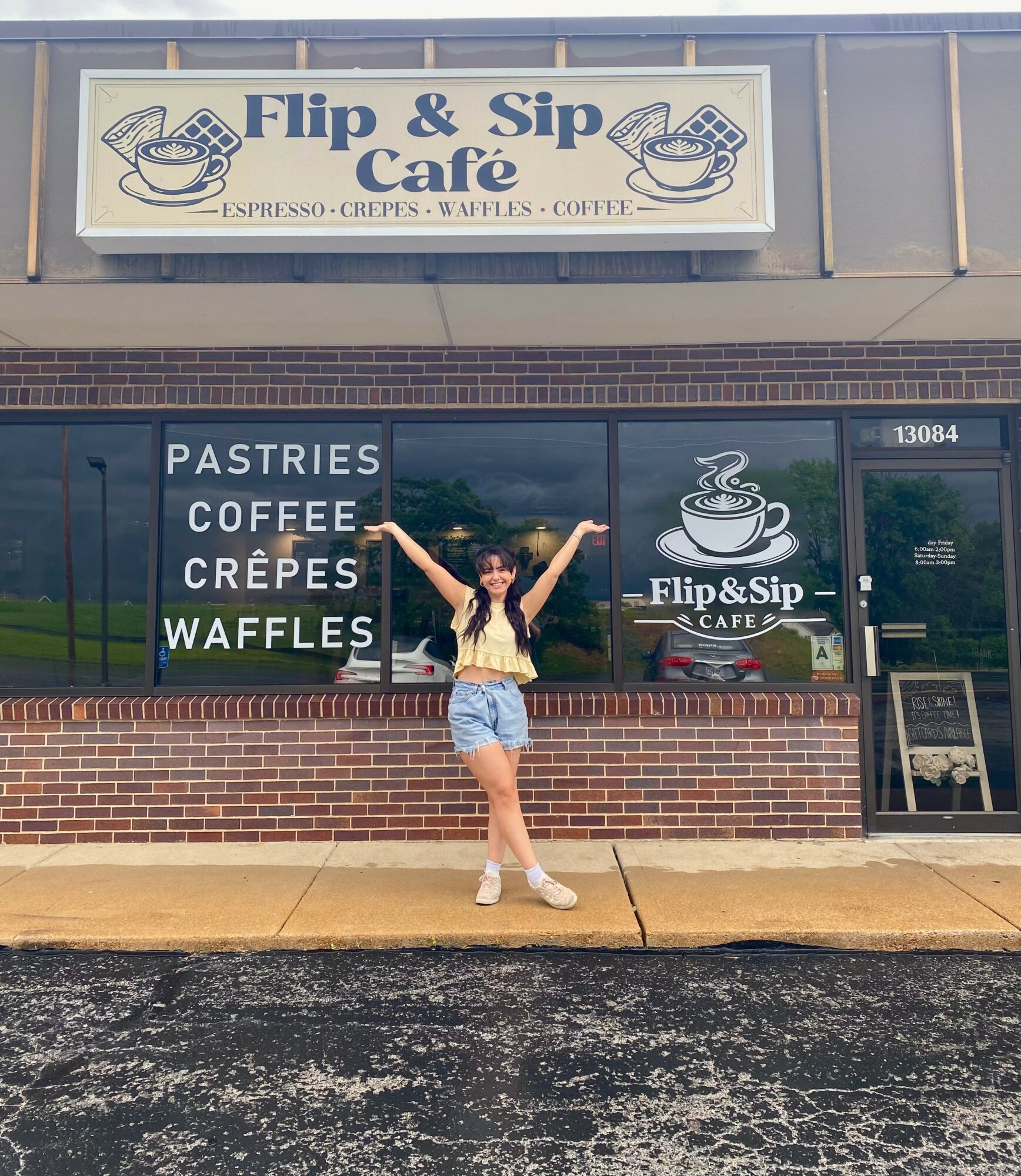 Person standing outside Flip & Sip Café with arms raised, window display shows pastries, coffee, crepes, waffles, and café logo.