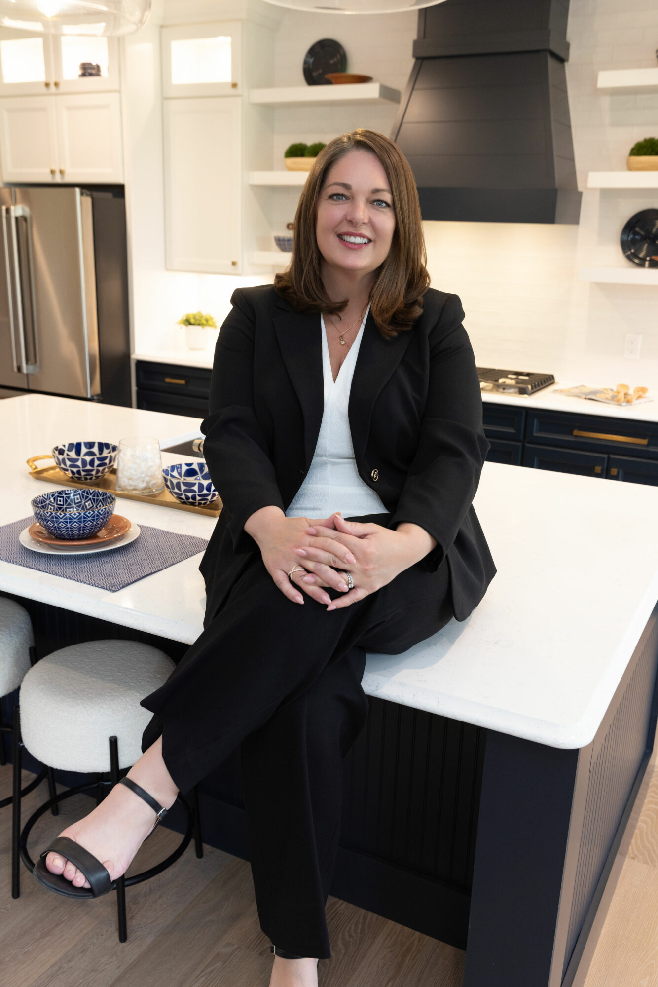 Woman sitting on kitchen counter, smiling, in a modern kitchen with white cabinets and black accents.