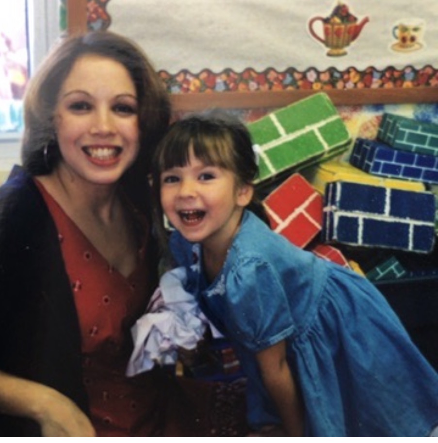 A woman and a young girl smiling, with colorful toy blocks in the background.