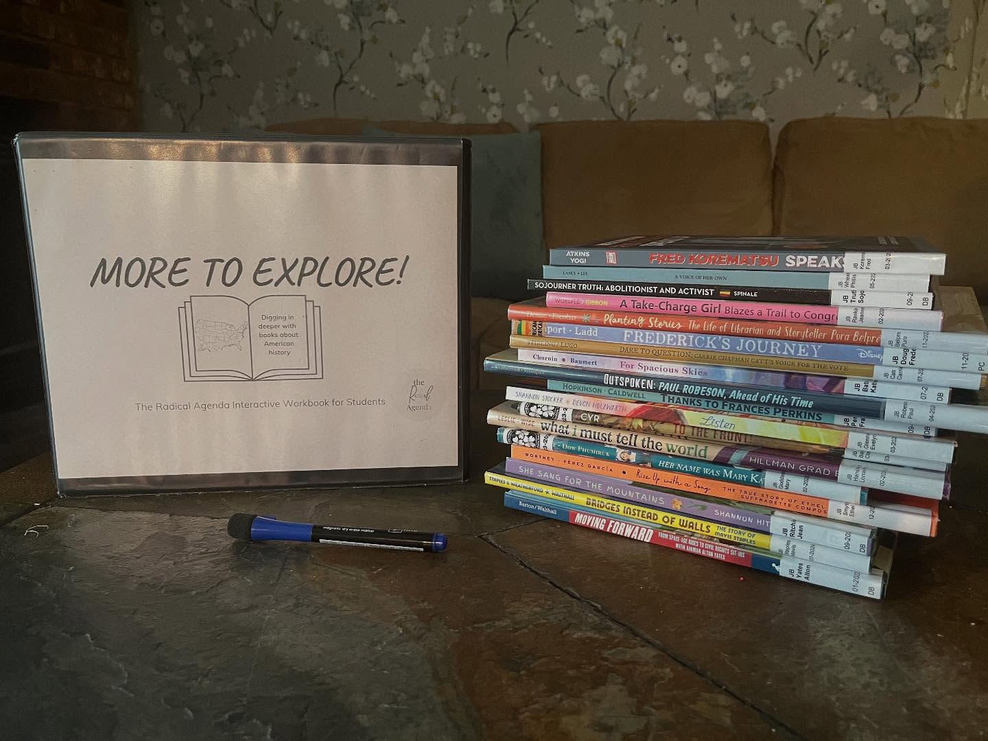 Stack of books on a table with a sign reading 'More to Explore!' and a pen nearby.