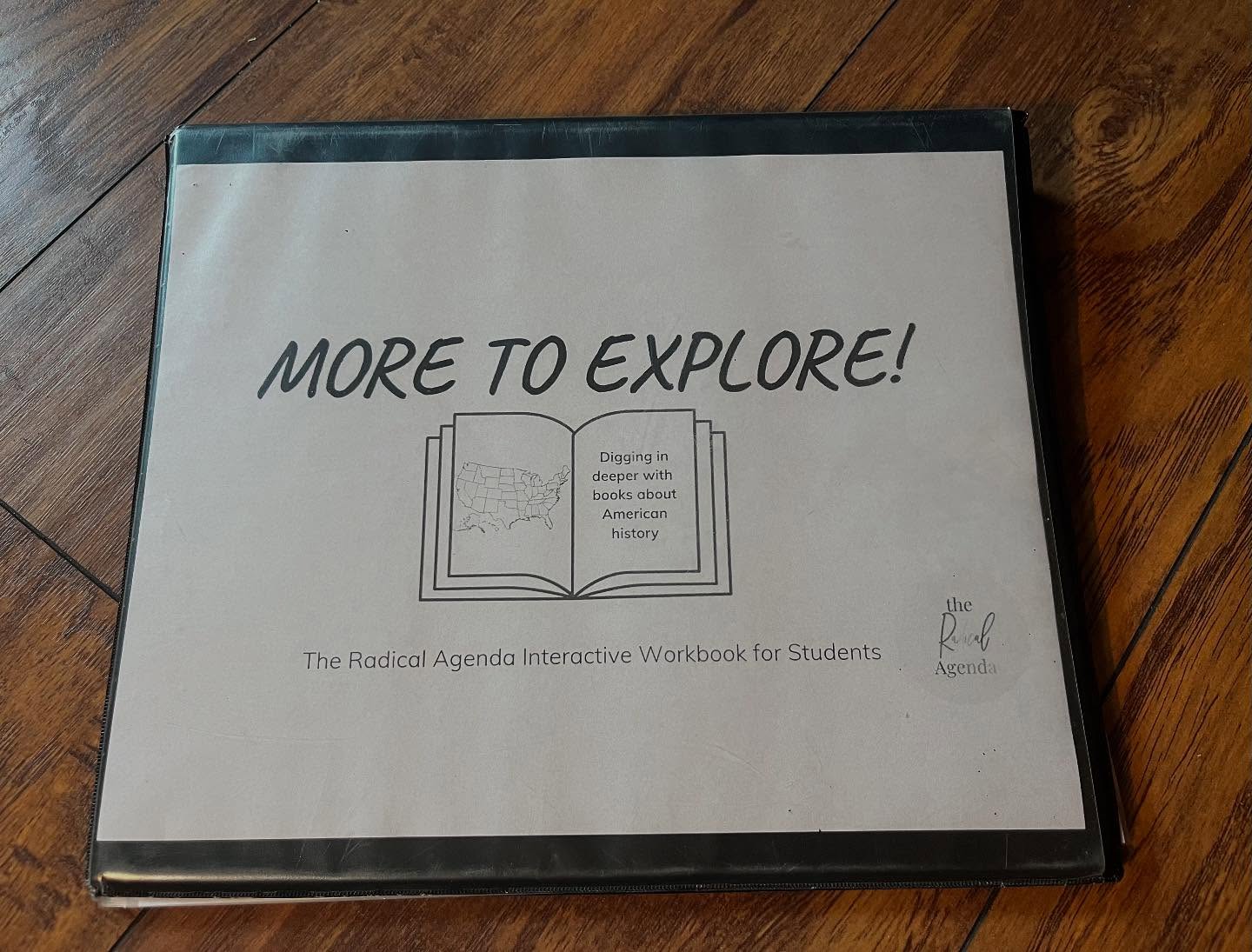 Box with a cover page titled 'MORE TO EXPLORE!' and an open book illustration, on a wooden surface.