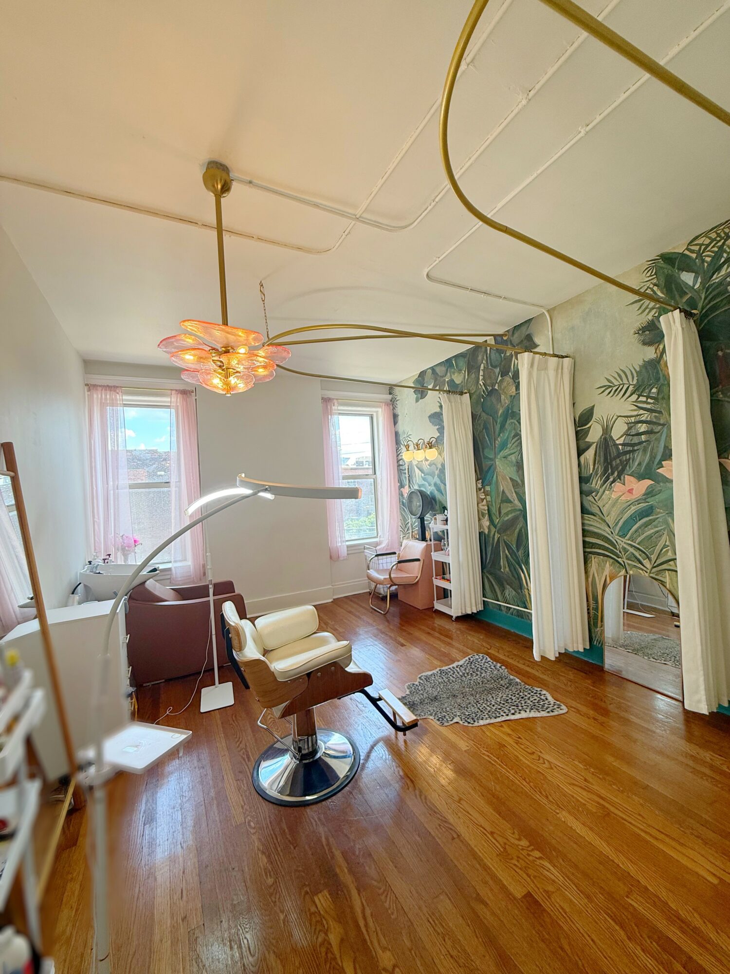 Room with large windows, wooden floor, vintage chair, and decorative curtains with tropical leaf pattern.