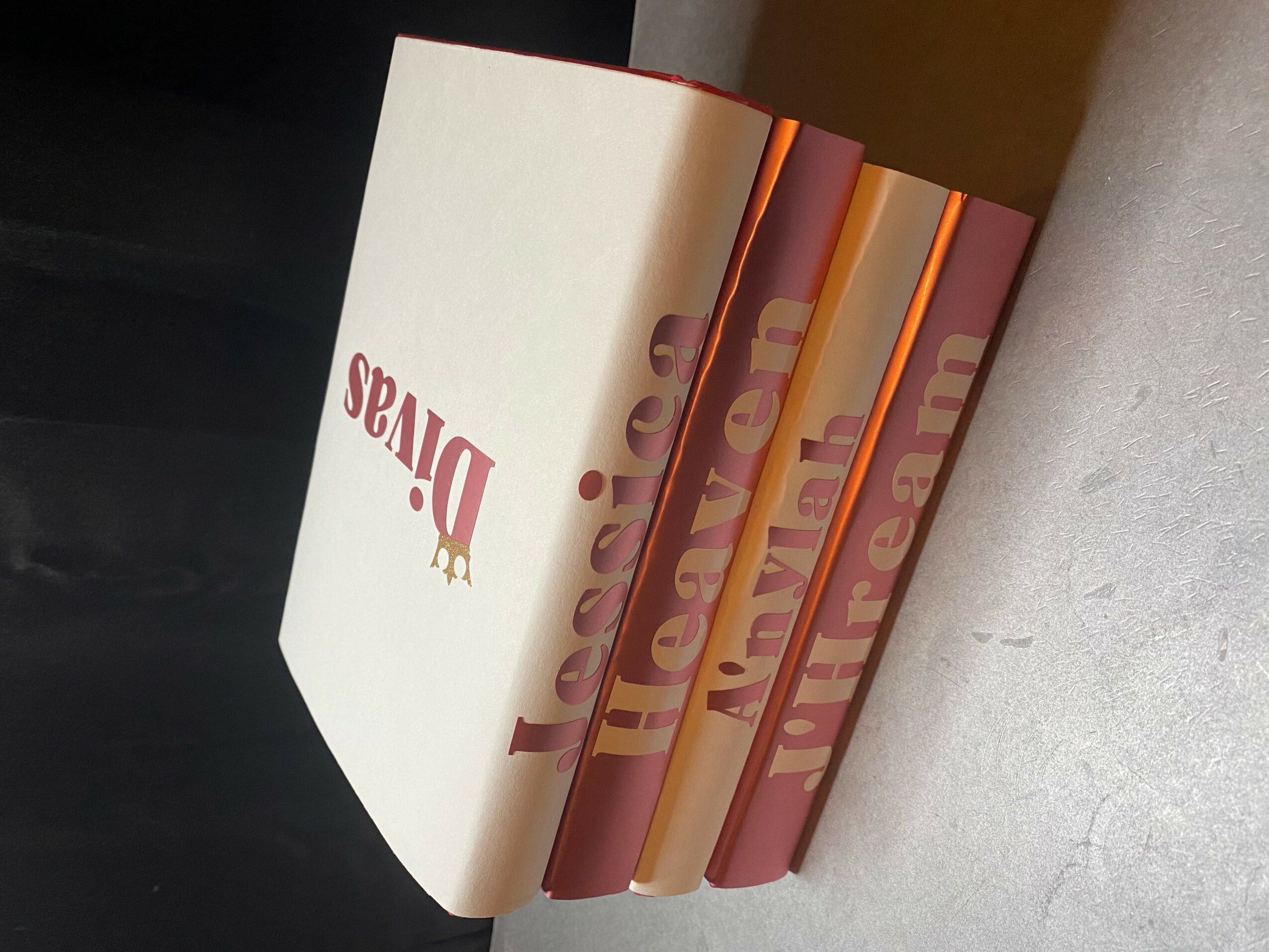 Five books stacked vertically with colorful spines, placed on a light surface, with a dark background.