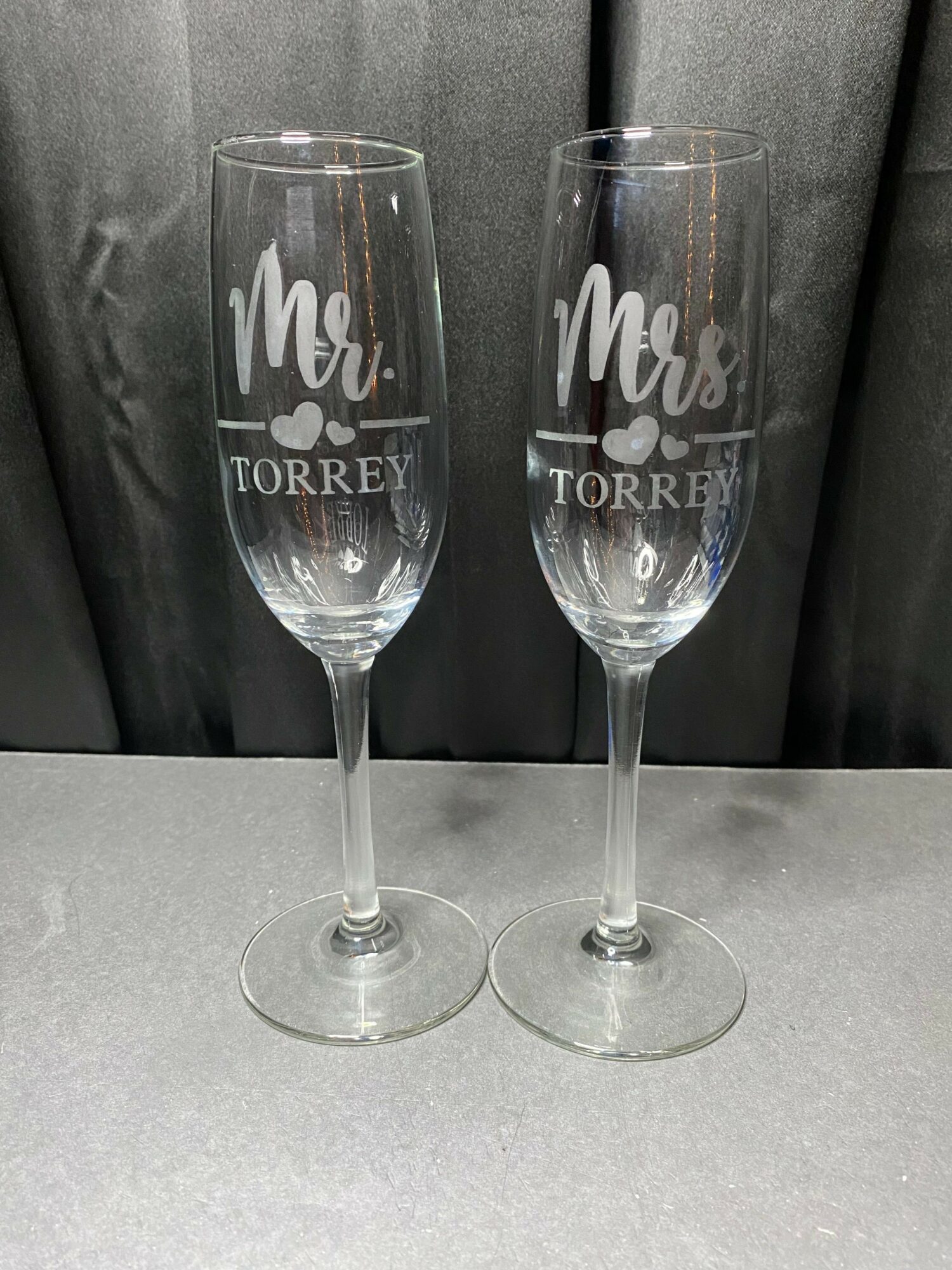 Two clear wine glasses with white text, placed on a gray surface, against a dark background.