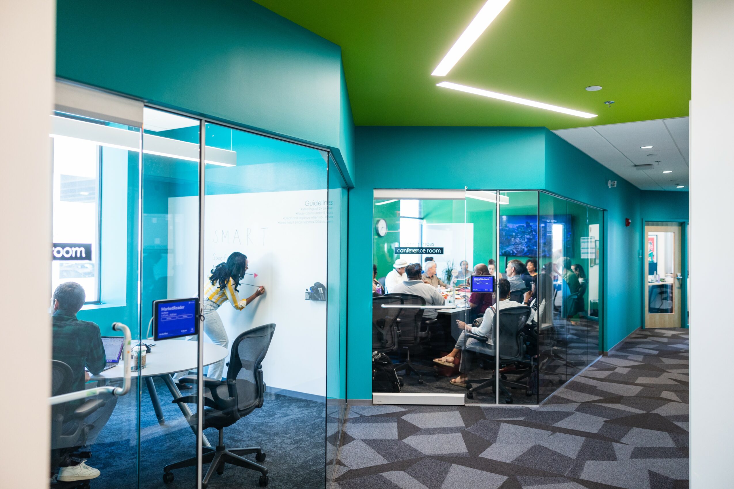 Office space with glass walls, people working at desks, and a colorful interior with green ceiling and blue walls.