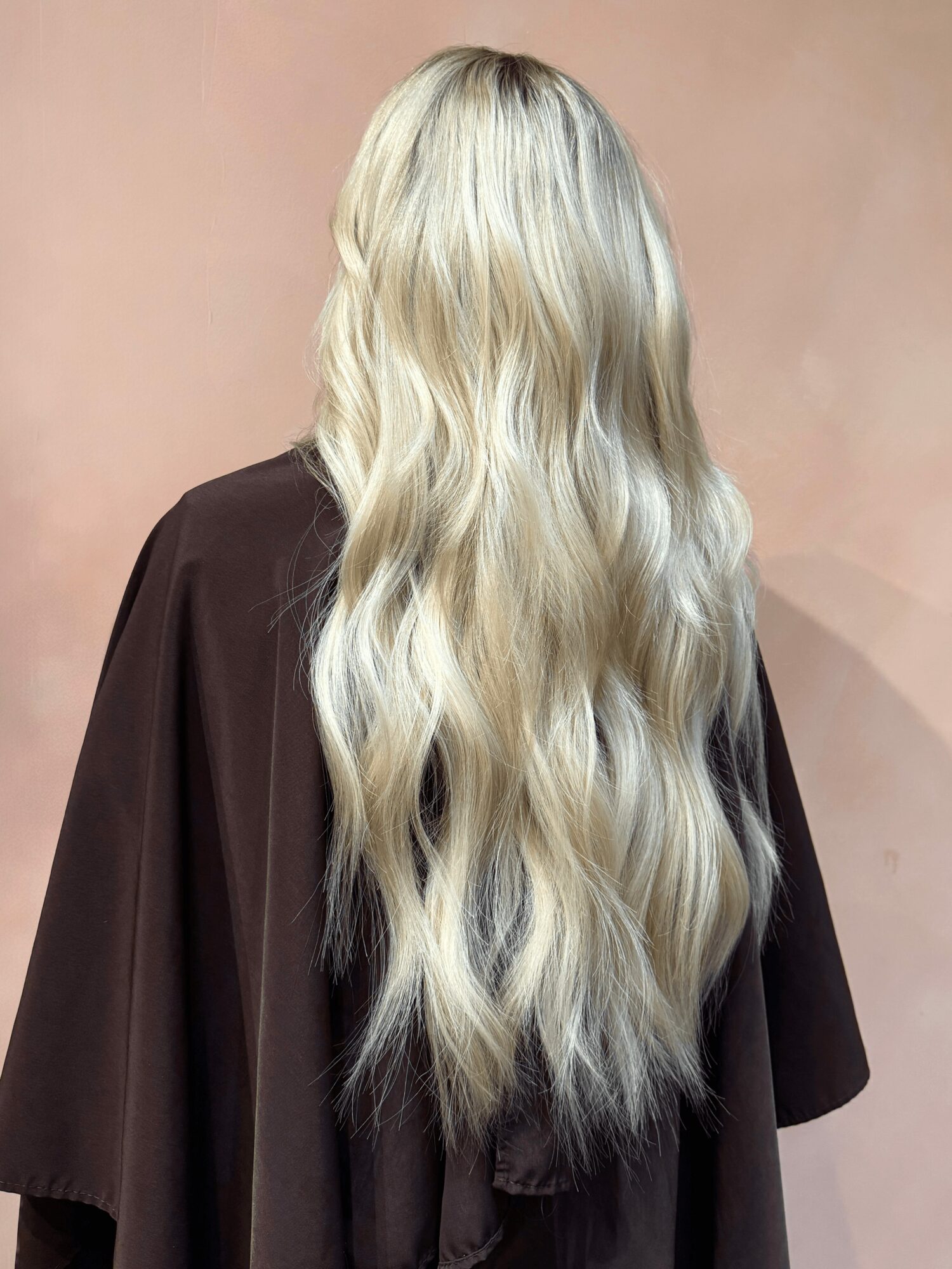 Back view of a person with long, wavy blonde hair wearing a dark brown garment.