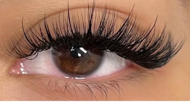 Close-up of a brown eye with long, curled eyelashes and well-defined eyelid makeup.