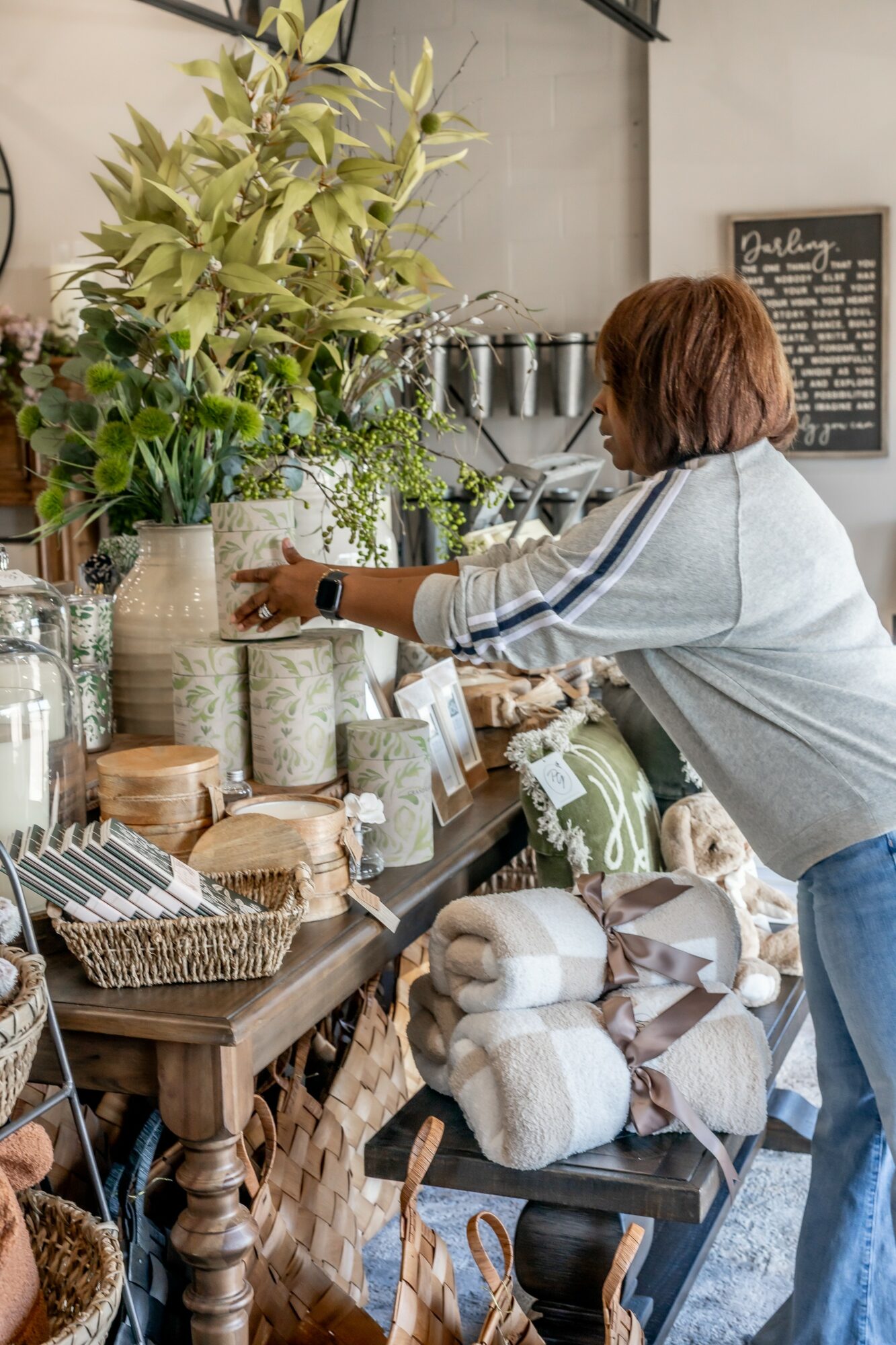 Woman shopping for home decor items at a store with plants, jars, and textiles on display.