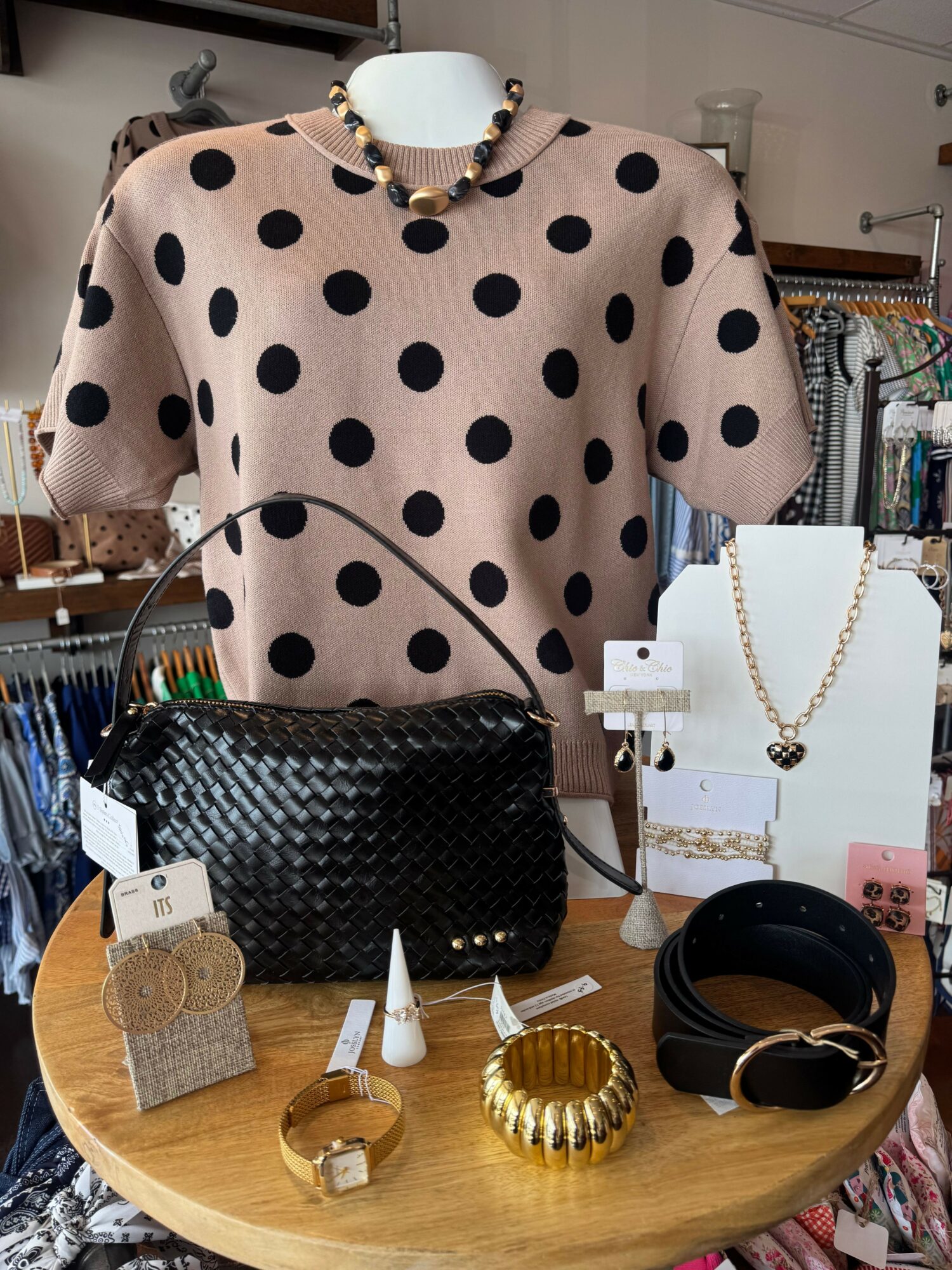 Display of jewelry including necklaces, bracelets, and a black woven clutch on a round wooden table.