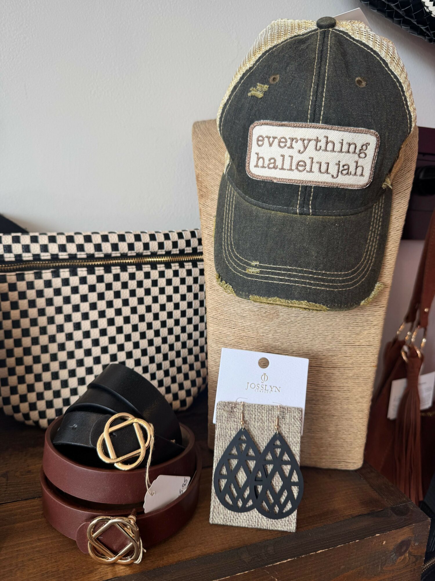 Decorative wall hanging with a quote, a checkered box, and a belt with a gold buckle on a wooden surface.