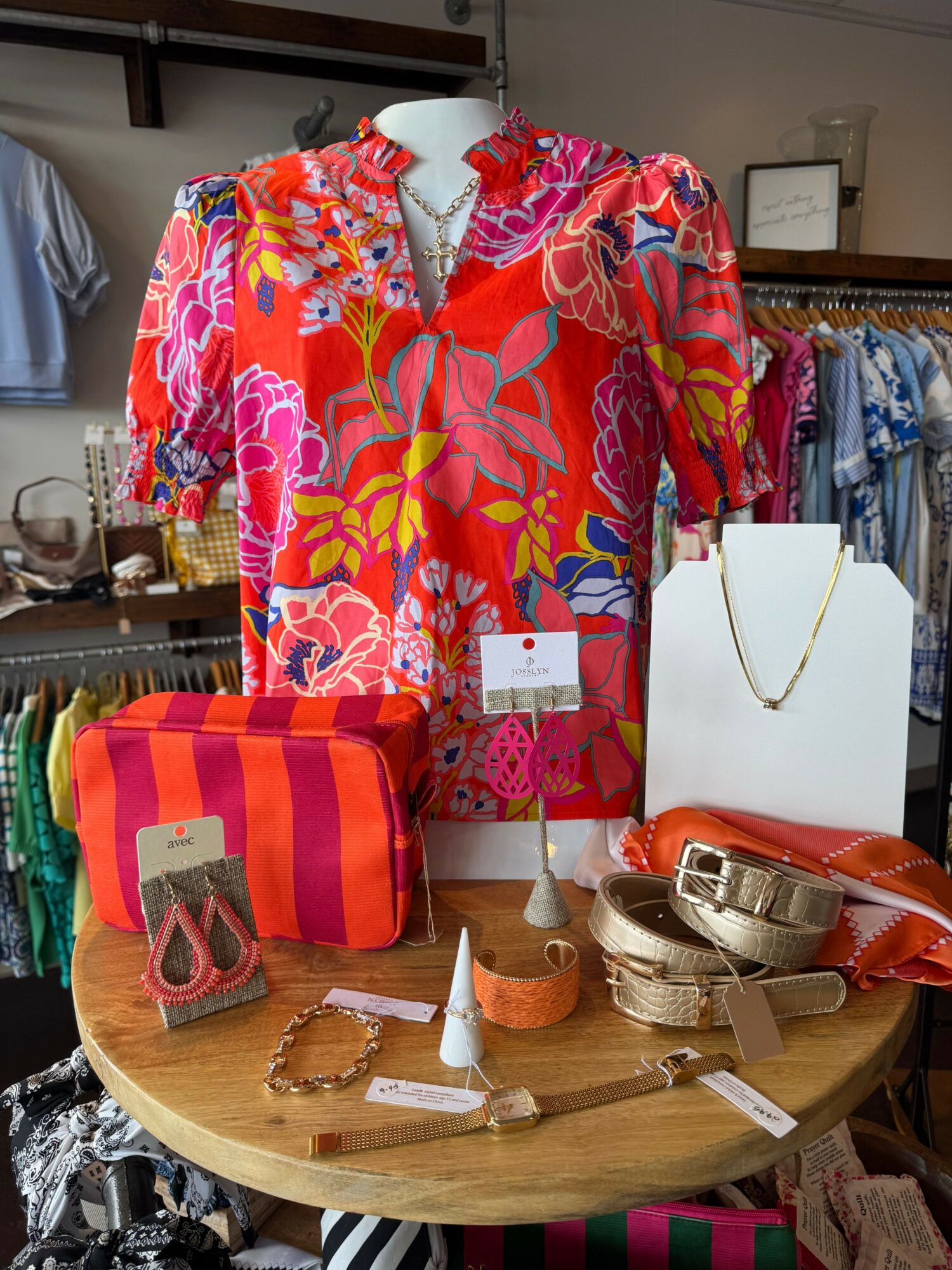 Display of colorful clothing, handbags, and accessories on a round table in a store.