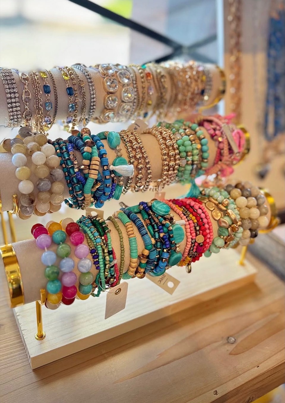 Display of colorful beaded and pearl bracelets on a wooden stand, arranged in rows with various designs and colors.