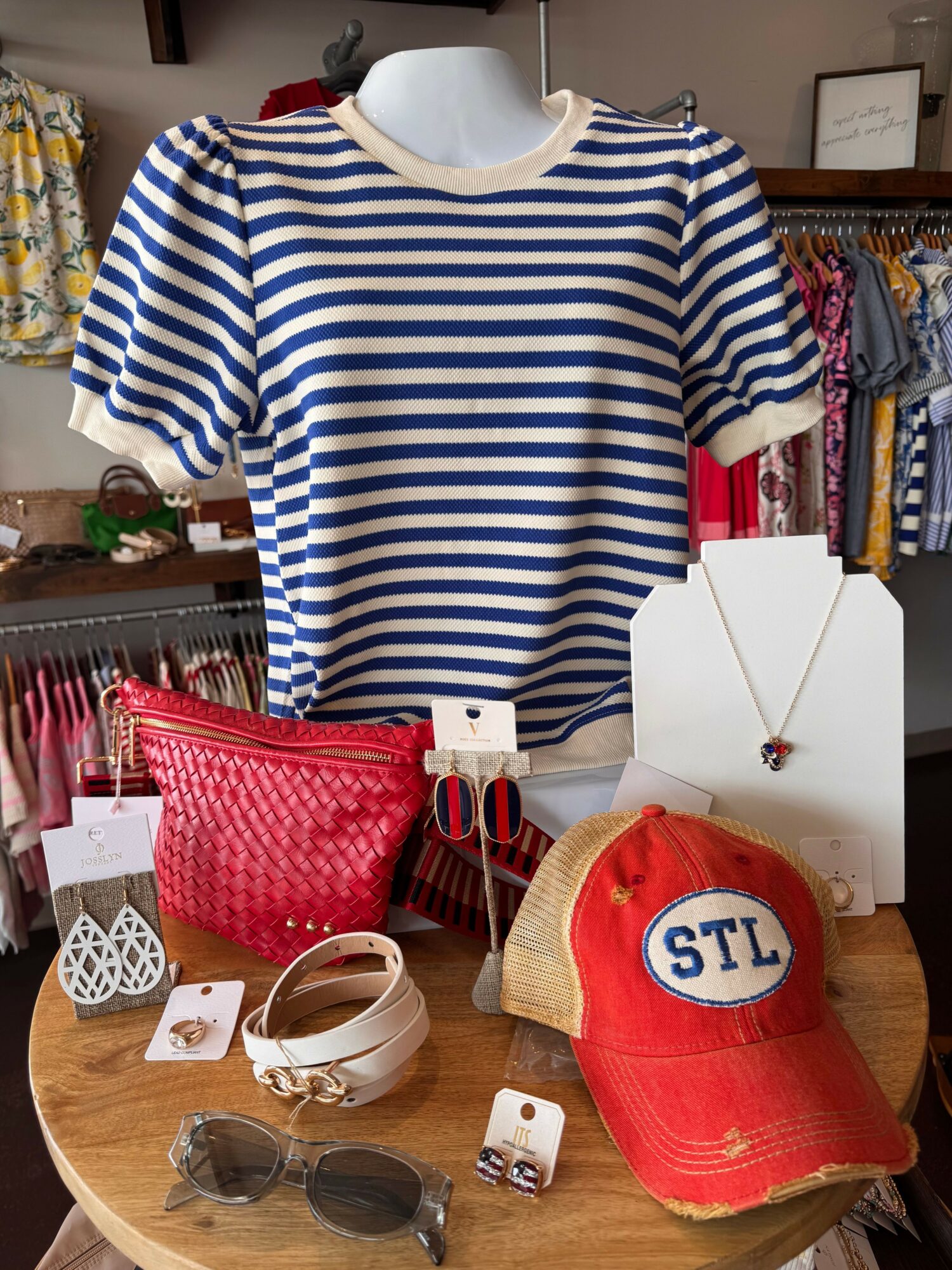 Striped shirt, red bag, hat, sunglasses, and accessories on a wooden table.