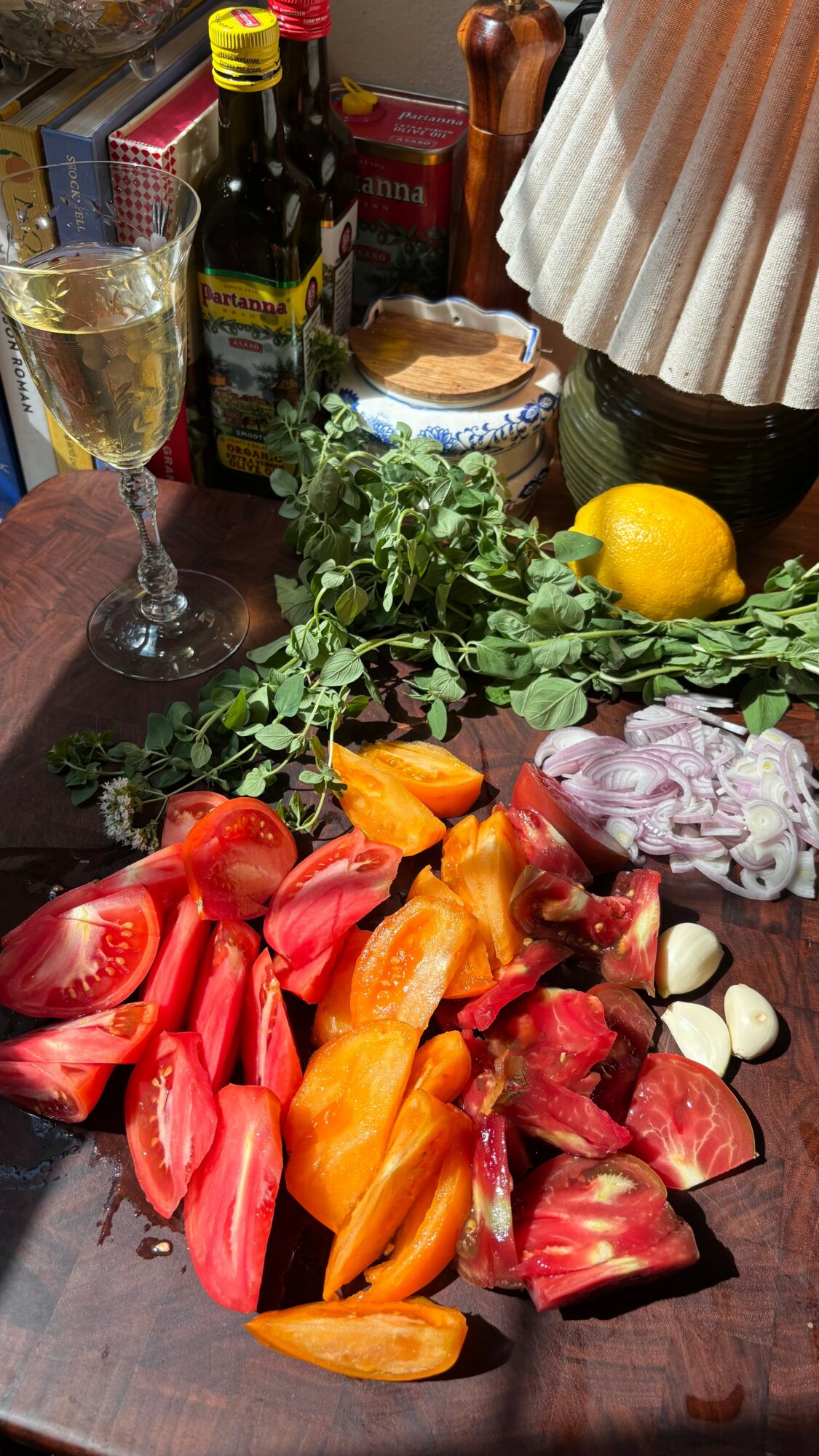 Cut tomatoes, peppers, and garlic on a dark wooden table with a lemon, herbs, and bottles in the background.