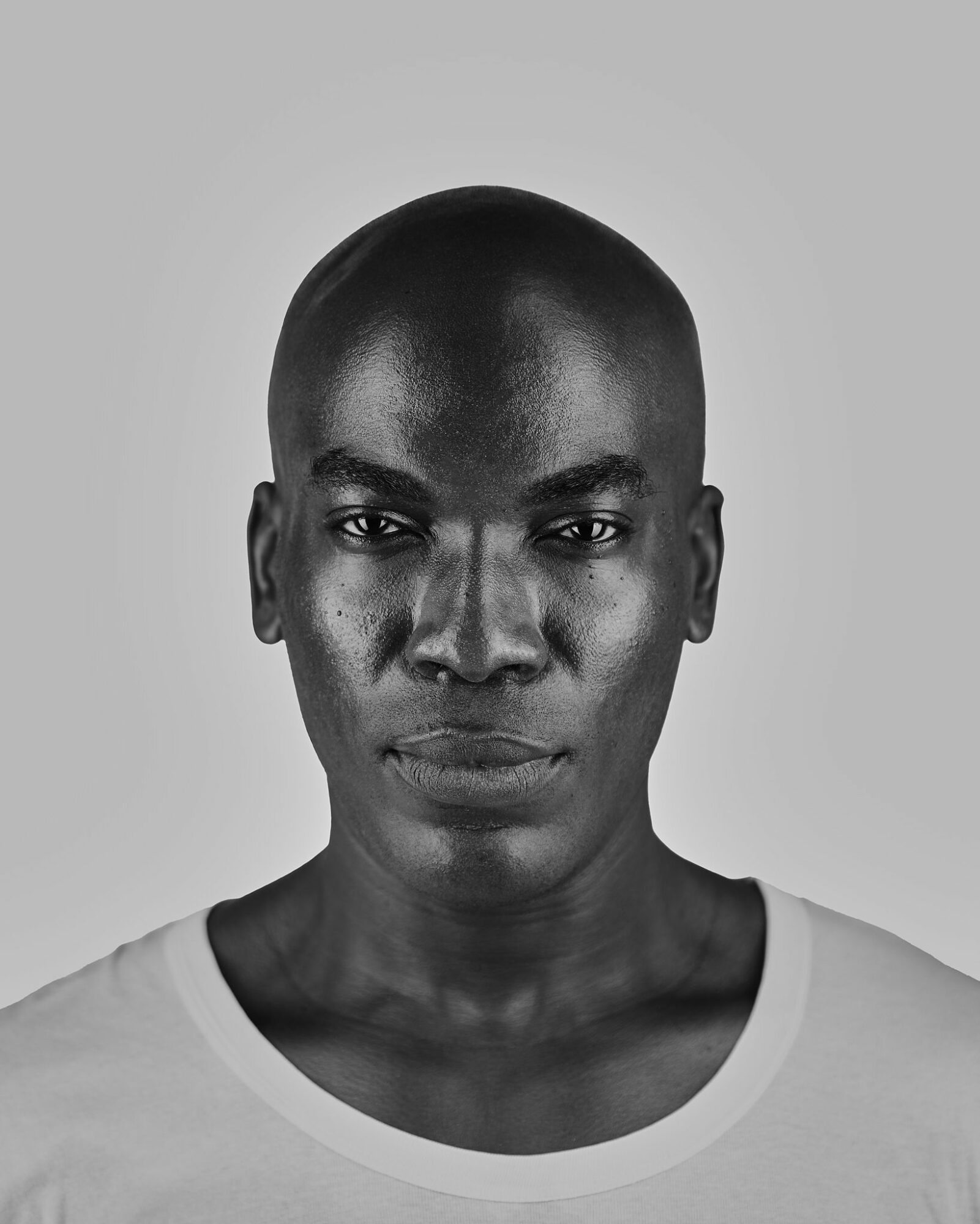 Portrait of a person with a shaved head and serious expression, facing forward, in black and white.