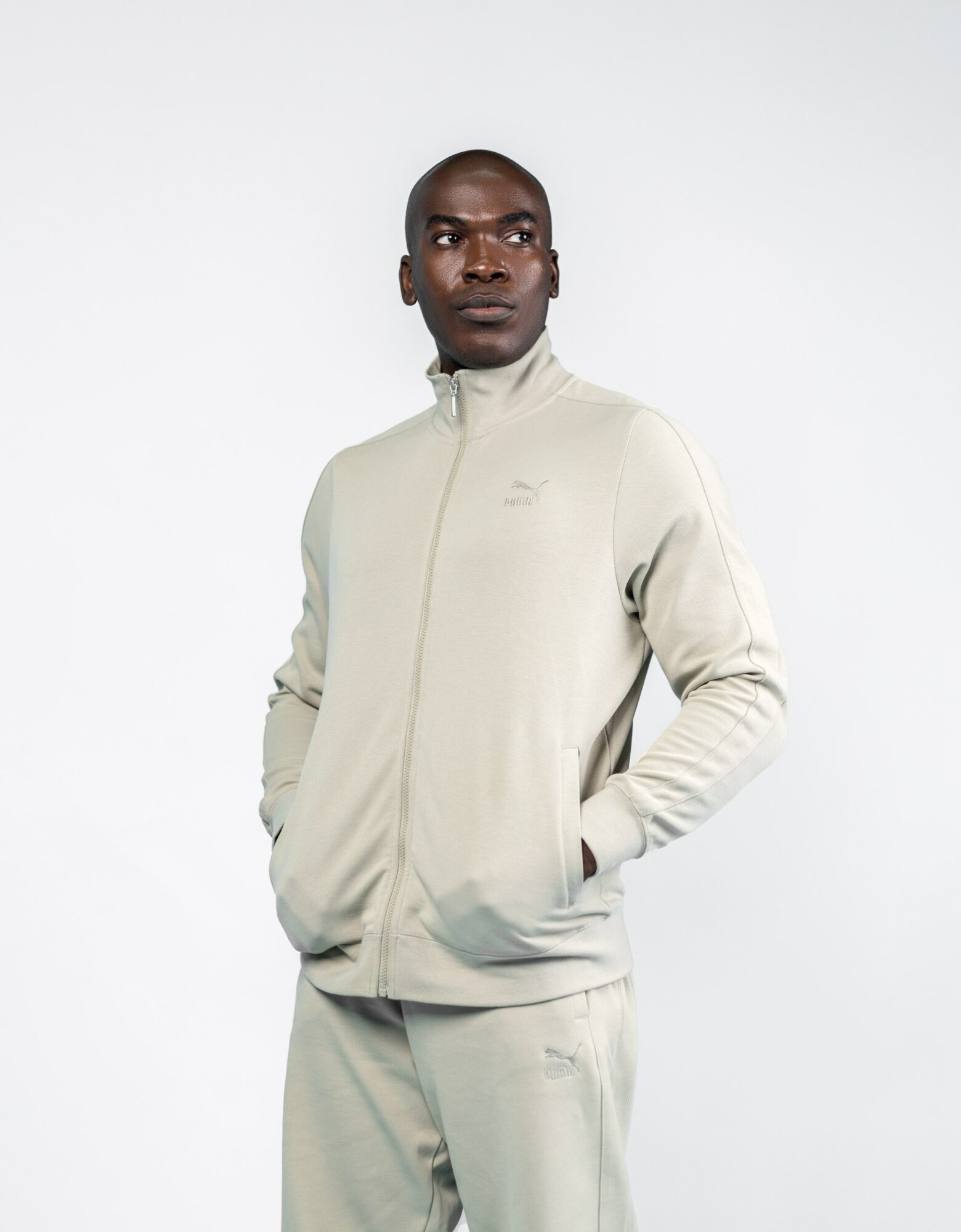 Man in light-colored tracksuit with hands in pockets, standing against a plain white background.