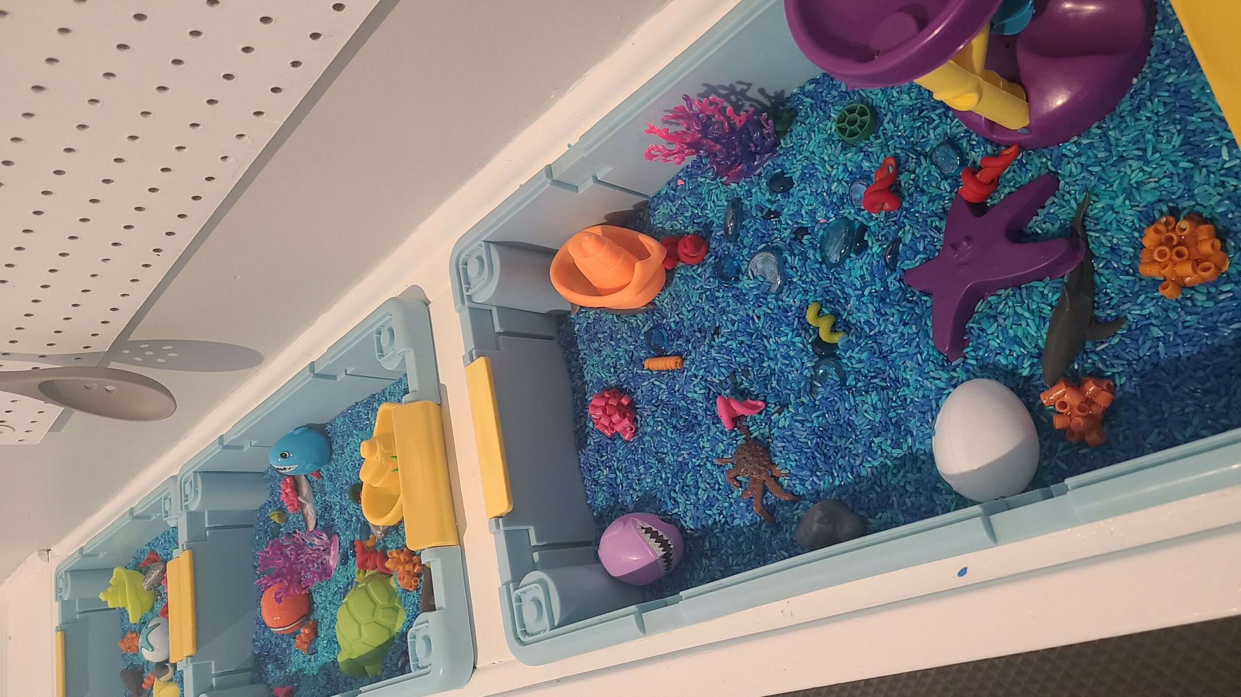 Two plastic containers filled with colorful toy sea creatures and accessories on a blue textured surface.