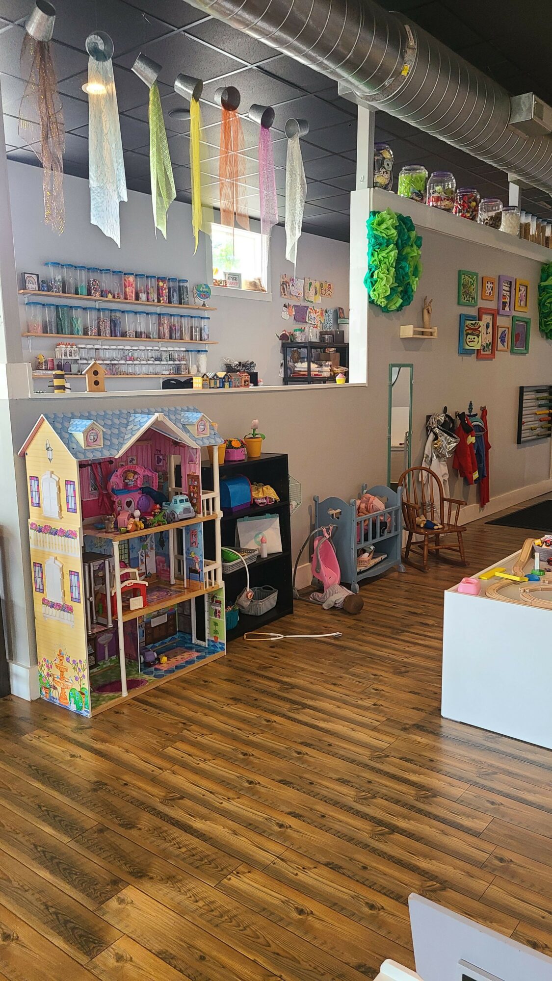 Children play in a colorful indoor play area with wooden flooring and various toys and structures.
