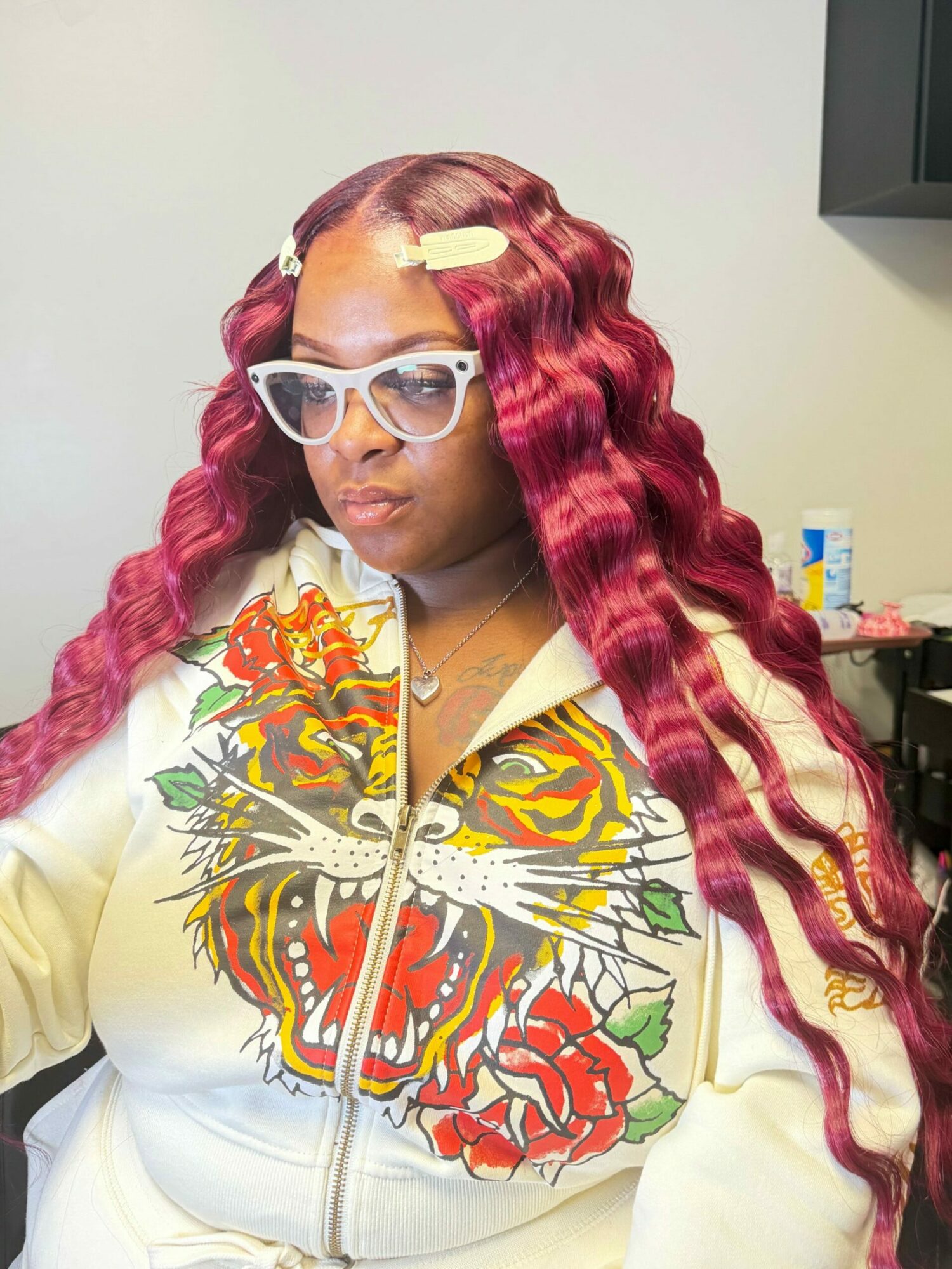 Woman with long, wavy red hair, wearing glasses and a colorful butterfly and floral design on her white hoodie.