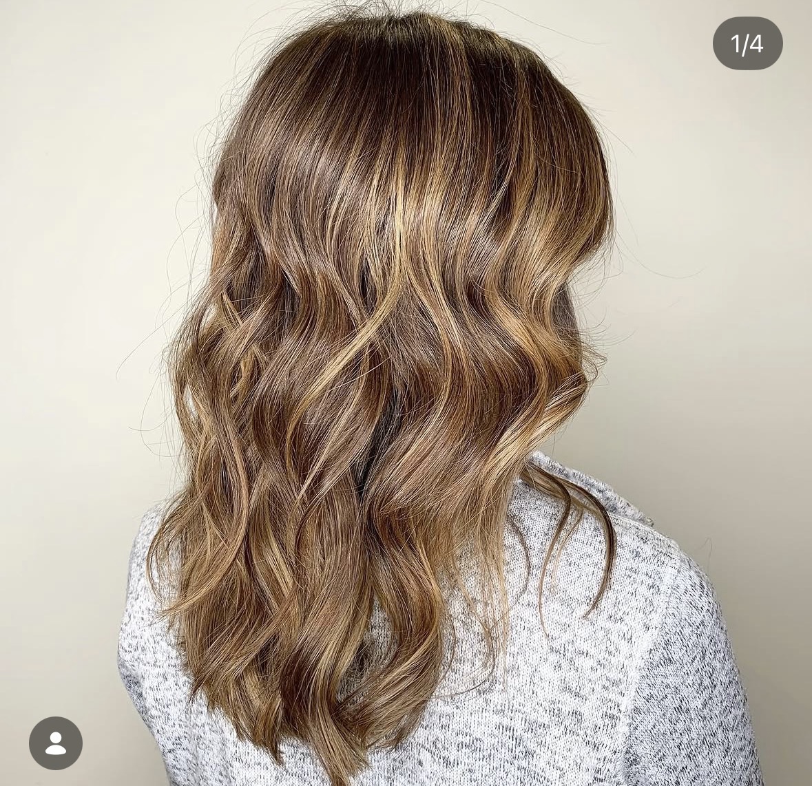 Back view of a person with wavy, light brown hair, wearing a gray sweater, against a plain background.
