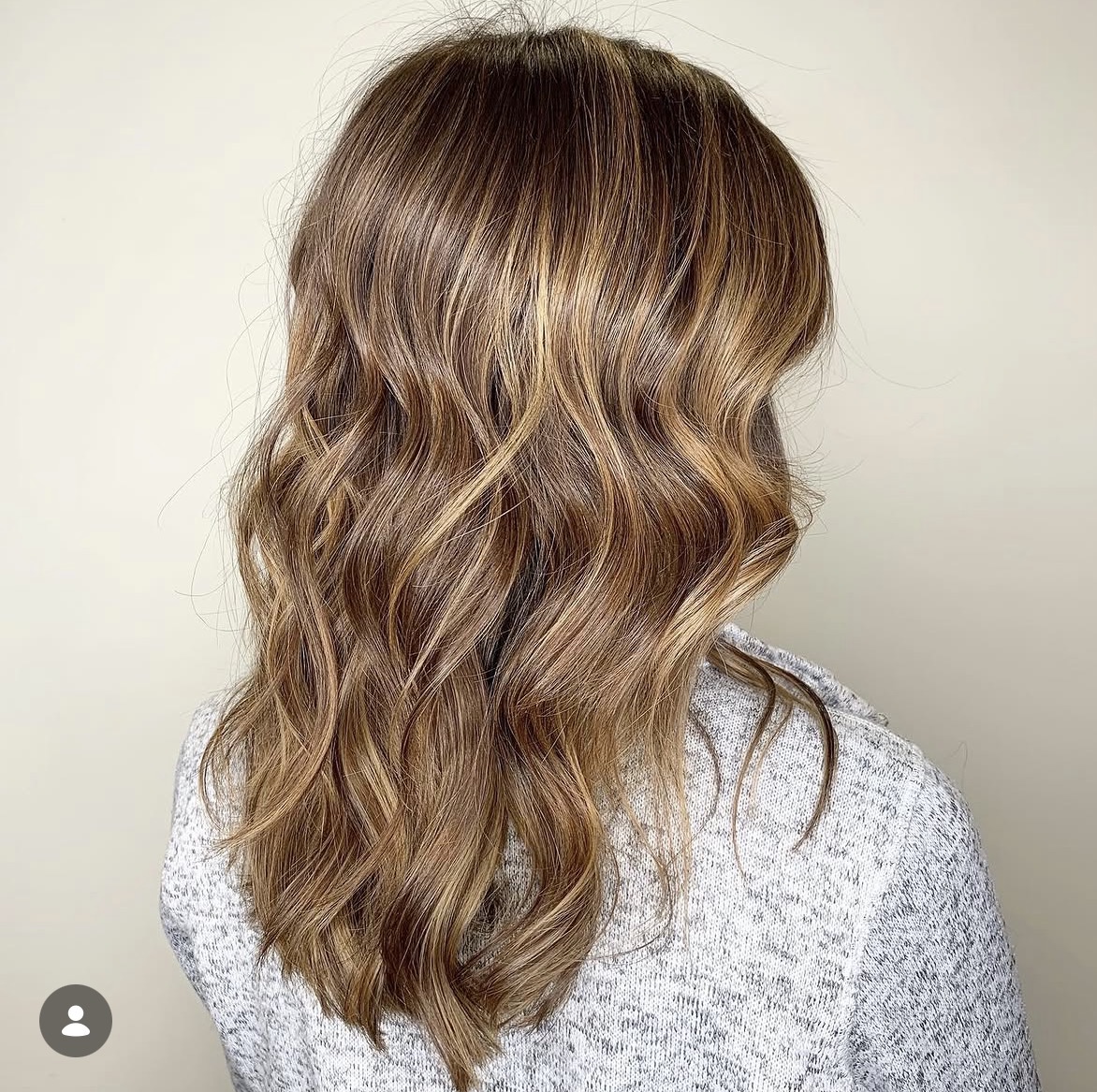 Back view of wavy, light brown hair with subtle highlights, shoulder length, against a plain background.