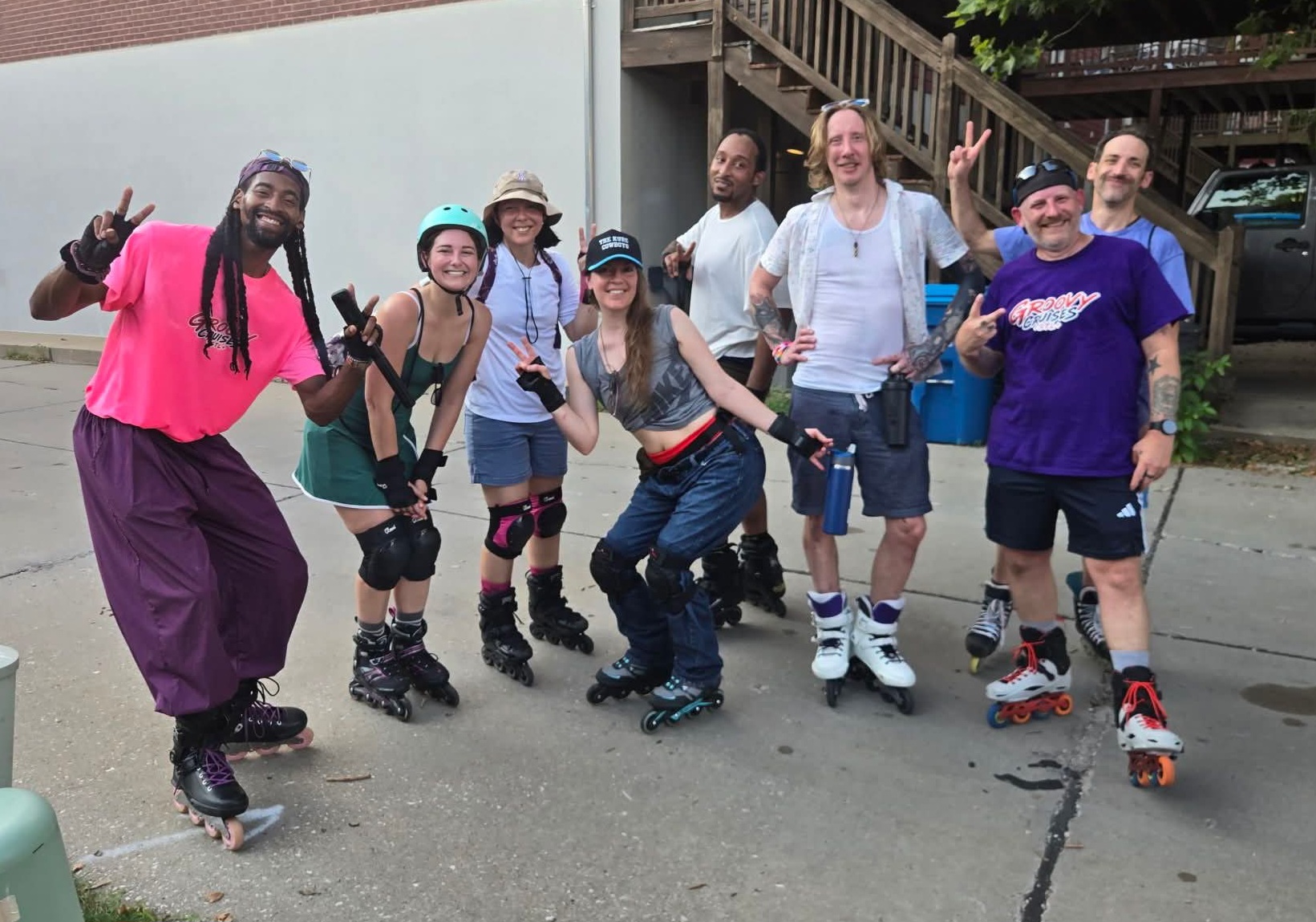 Group of nine people wearing roller skates, smiling and posing outdoors on a paved surface.