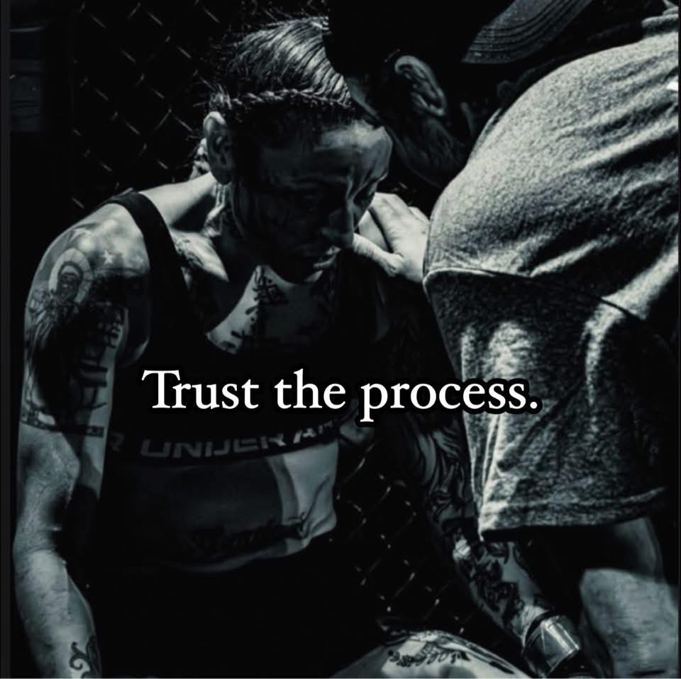 Two people in a dark setting, one with tattoos, with the text 'Trust the process.'