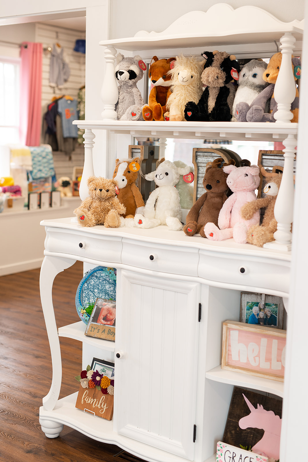 White shelf filled with stuffed animals, books, and toys in a cozy room with pink curtains and a window.