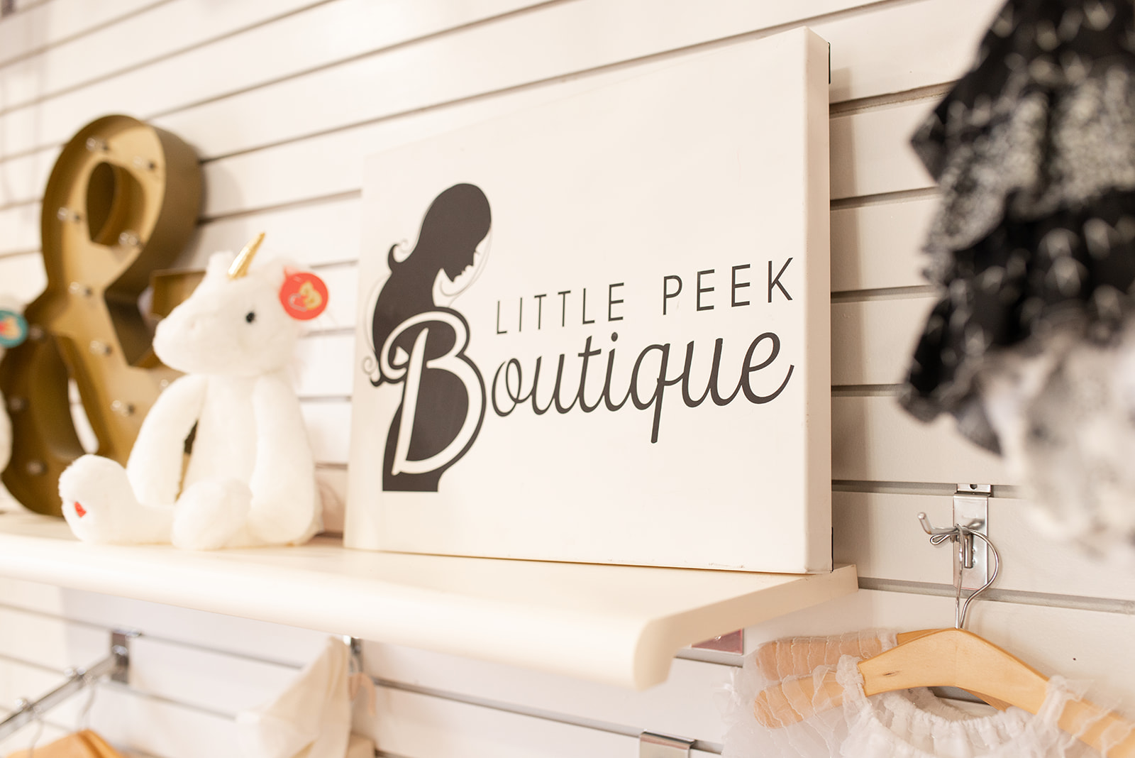 Sign reading 'Little Peek Boutique' with a silhouette of a girl, displayed on a wall with toys nearby.