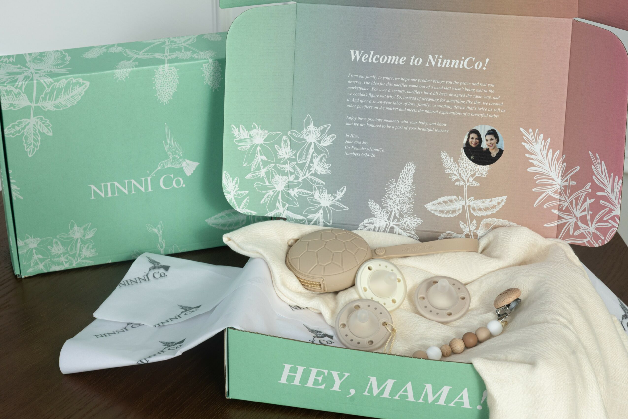 Open box with skincare products and a cloth, boxes in pastel colors with floral designs, text on boxes and booklet, on a dark surface.