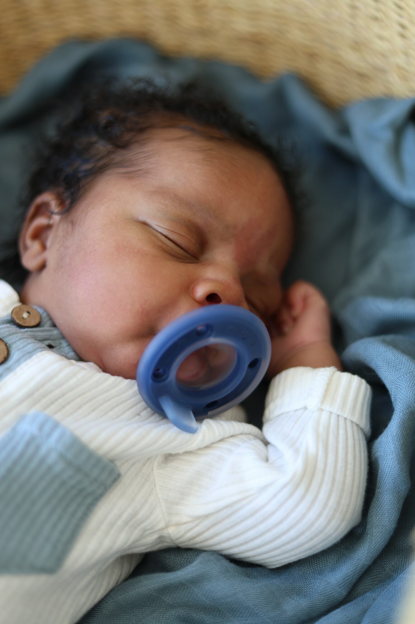 Close-up of a sleeping baby with a pacifier, lying on a soft surface, wearing a striped outfit.