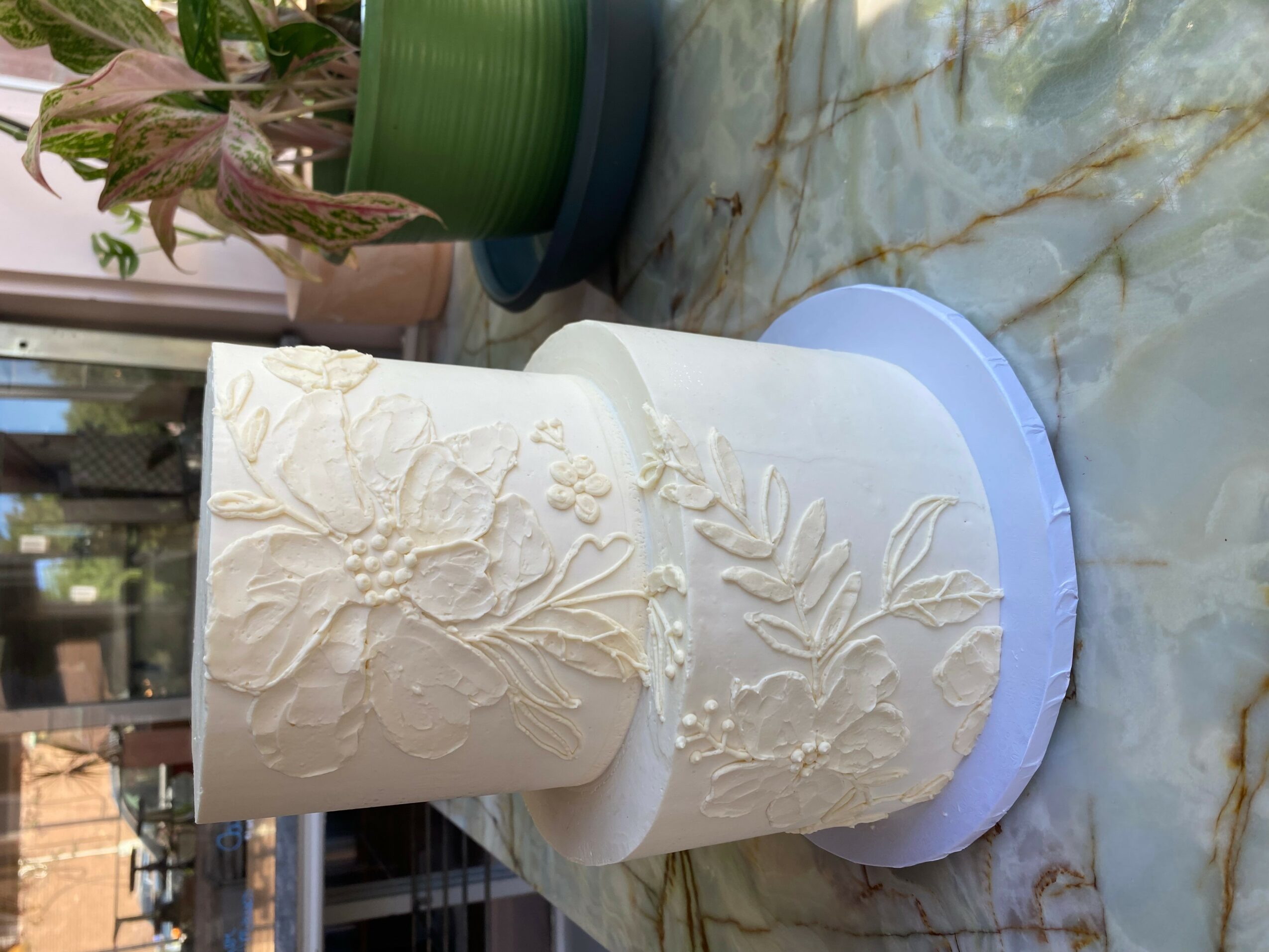 White cake with floral textured design on a round base, placed on a marble surface.
