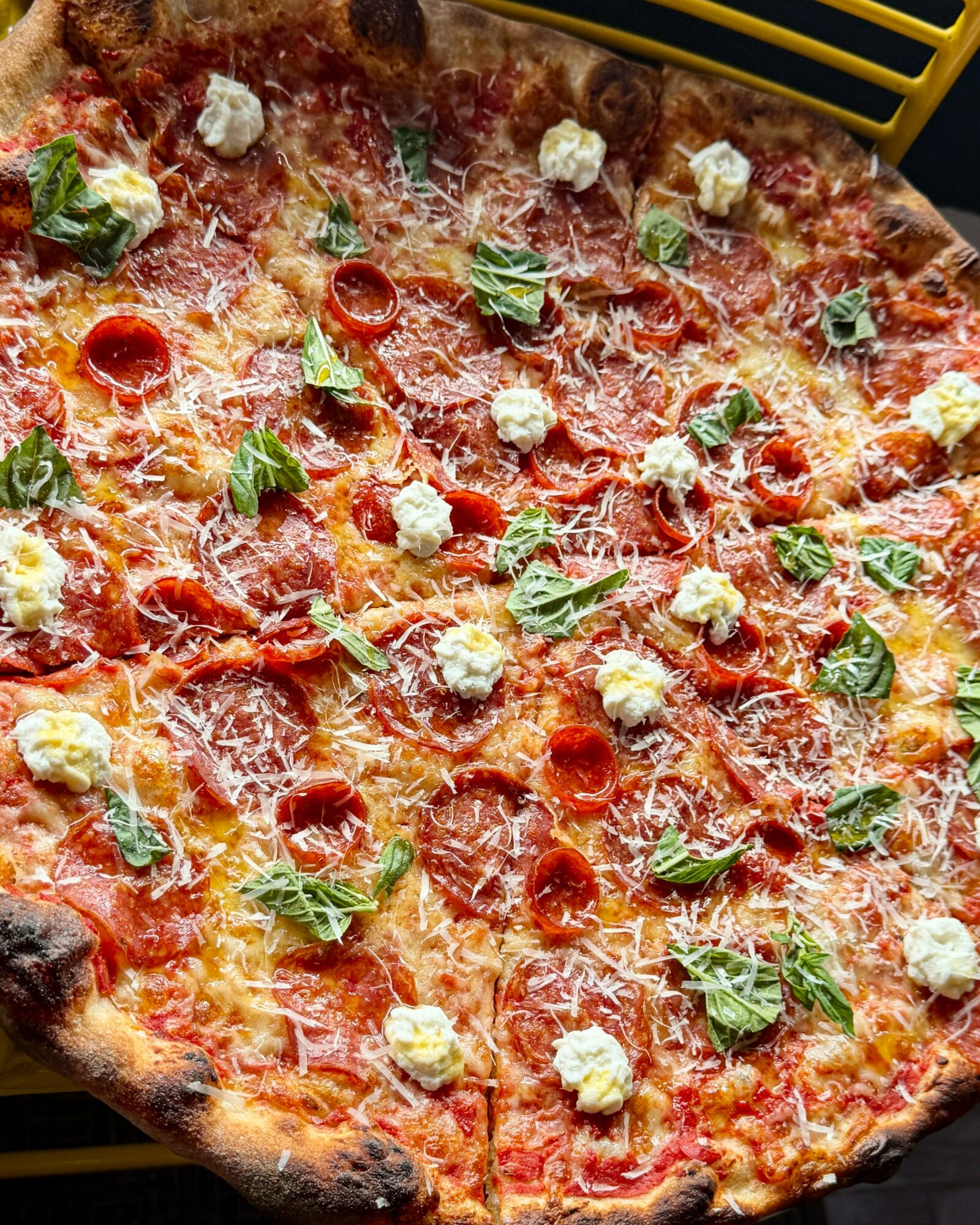 Large pizza topped with pepperoni, basil leaves, and dollops of cheese, with a golden crust.