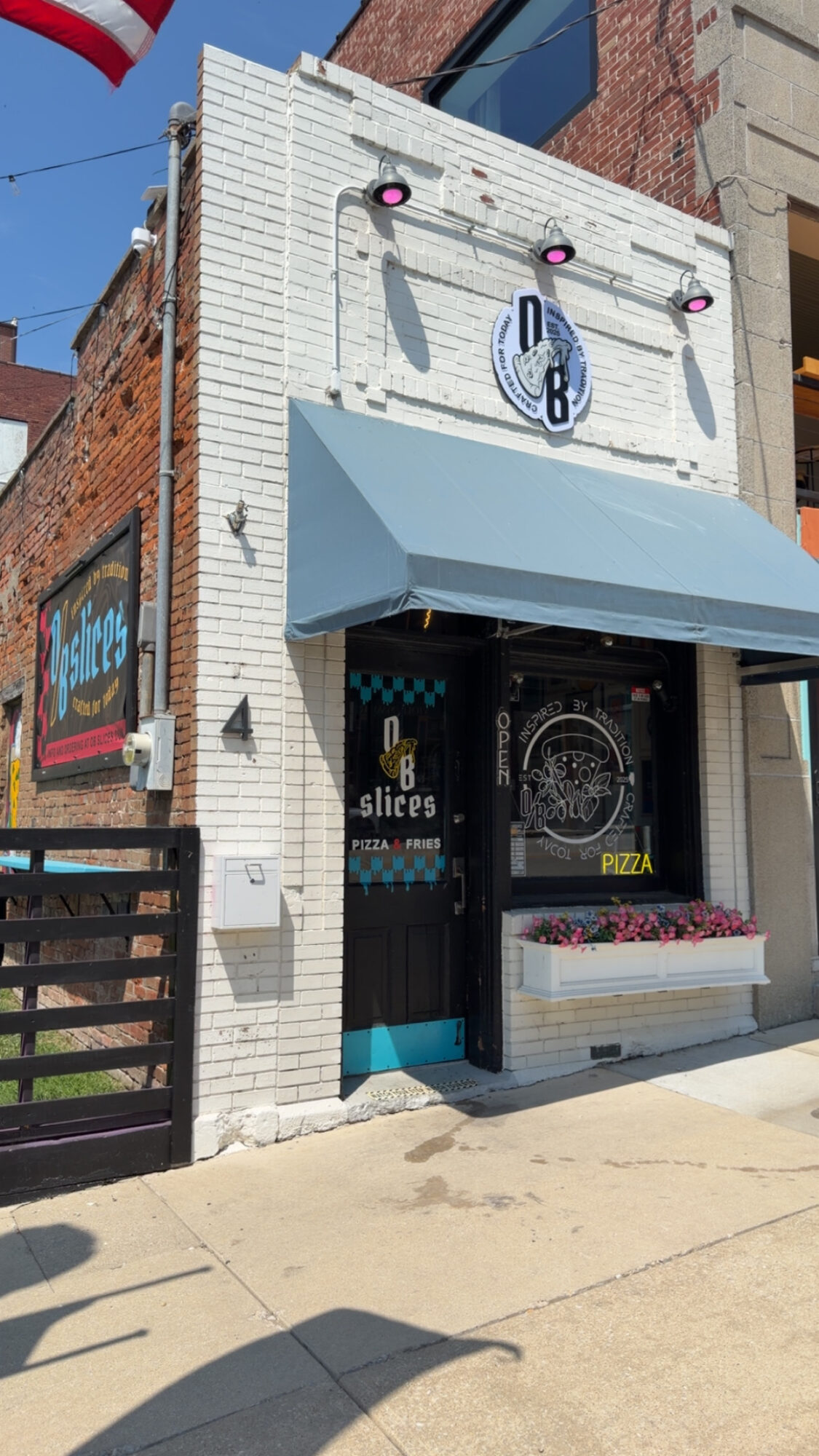 White brick storefront with a blue awning, circular sign, and a black door, located on a city street.