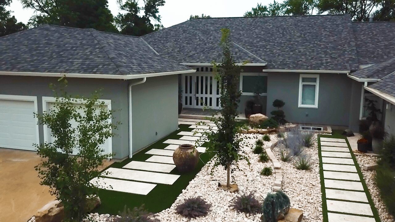 Front yard with pathway, trees, and landscaping in front of a house with a gray exterior and a garage.
