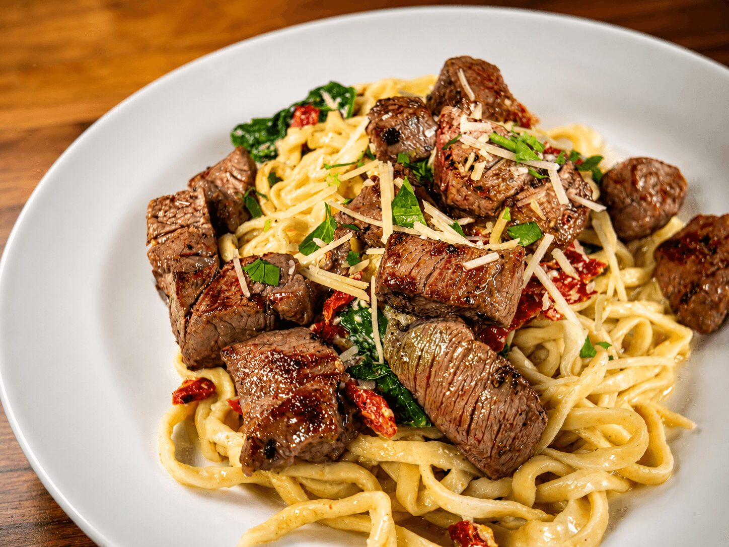 Plate of pasta with beef chunks, garnished with herbs and red pepper flakes, on a white dish.