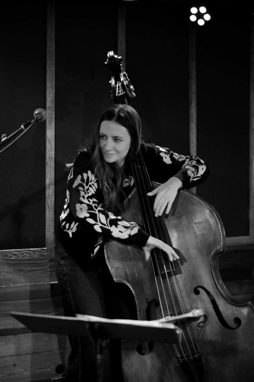 Woman playing a double bass on stage with microphones and lighting, in black and white.